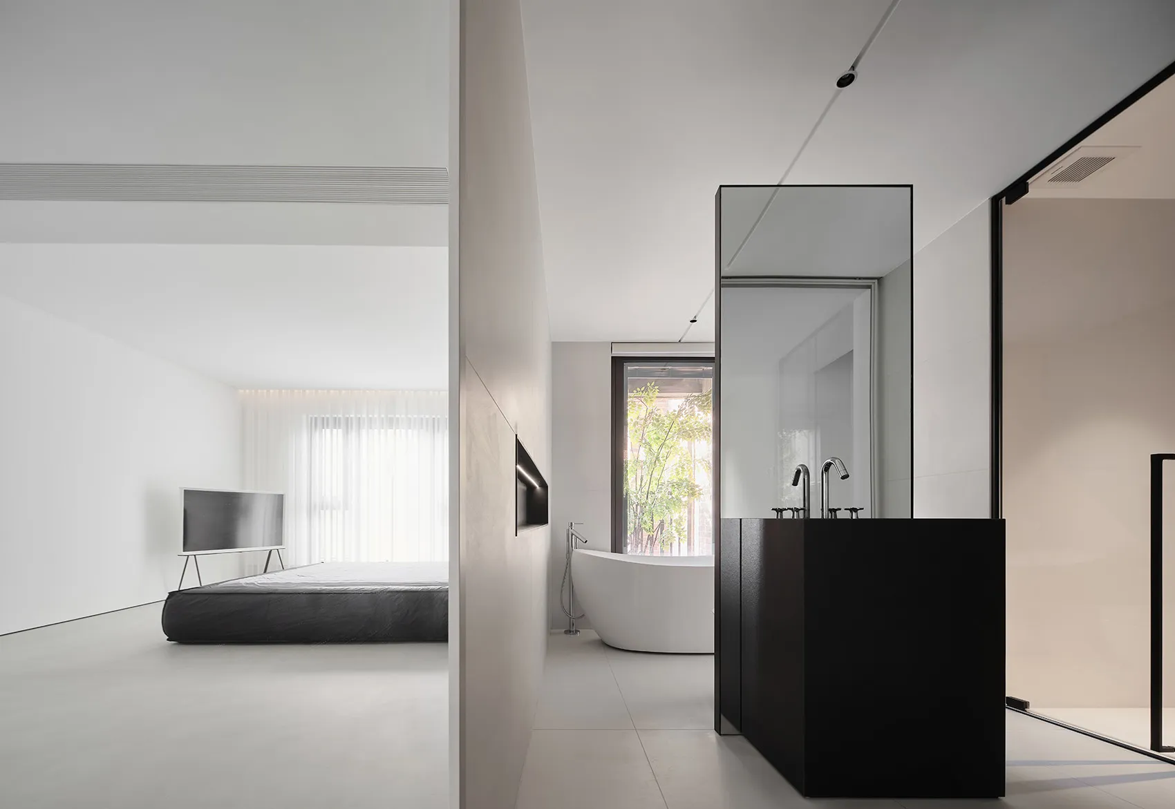 A minimalist interior design featuring a white concrete floor, black furnishings, and a modern bathroom setup.