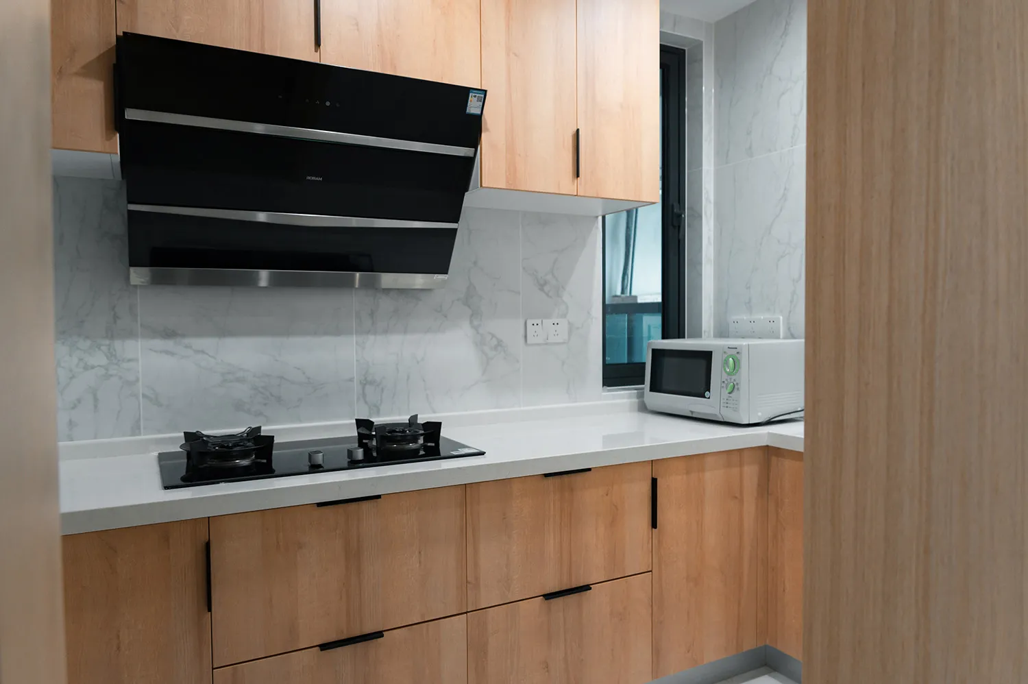 A minimalist kitchen with a white countertop, wooden cabinets, and modern appliances.
