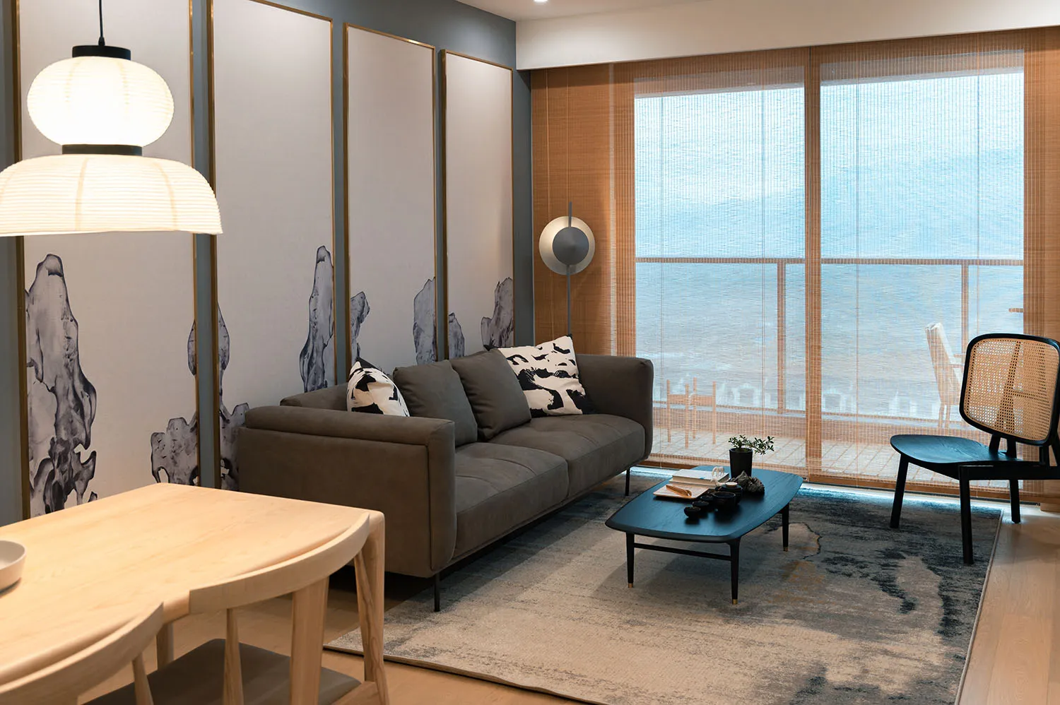 A modern living room with a gray sofa, black and white patterned pillows, and a wooden dining table with white chairs.