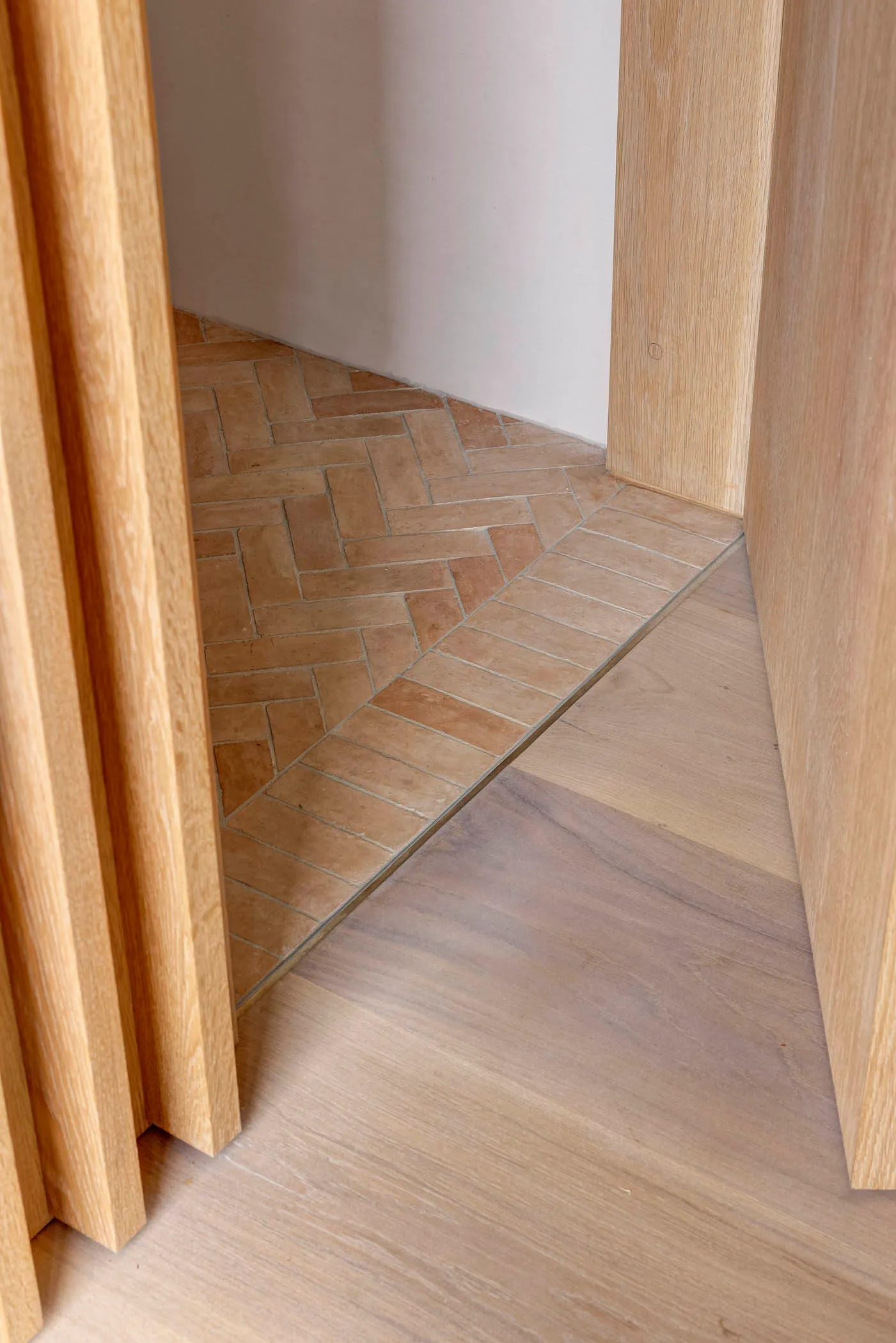 A wooden floor meets ceramic tiles in a transitional corner, showcasing a seamless blend of natural and modern materials.