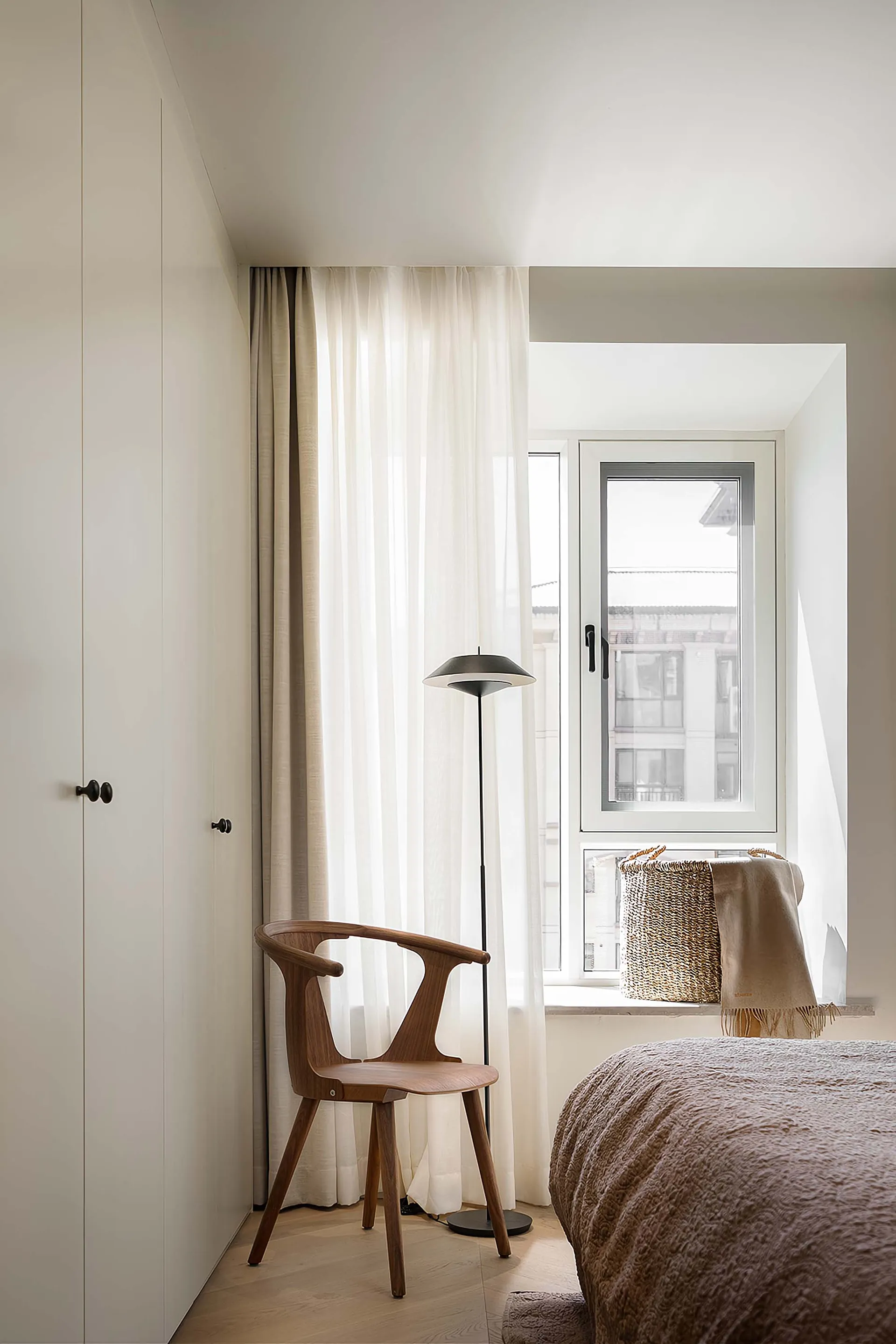 A minimalist bedroom featuring wooden furniture and a floor lamp.