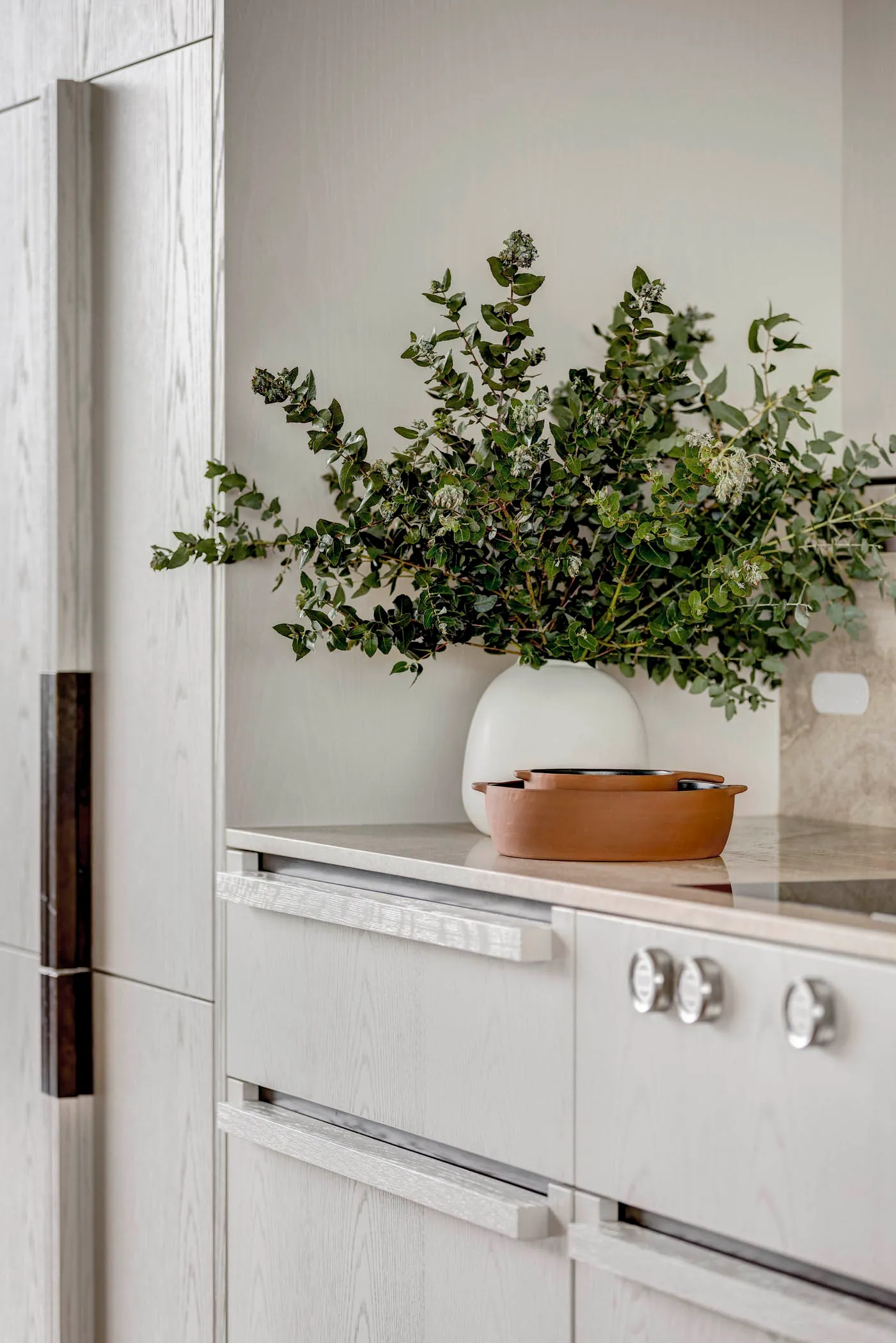 Modern minimalist kitchen featuring terracotta pots and a vase filled with greenery.