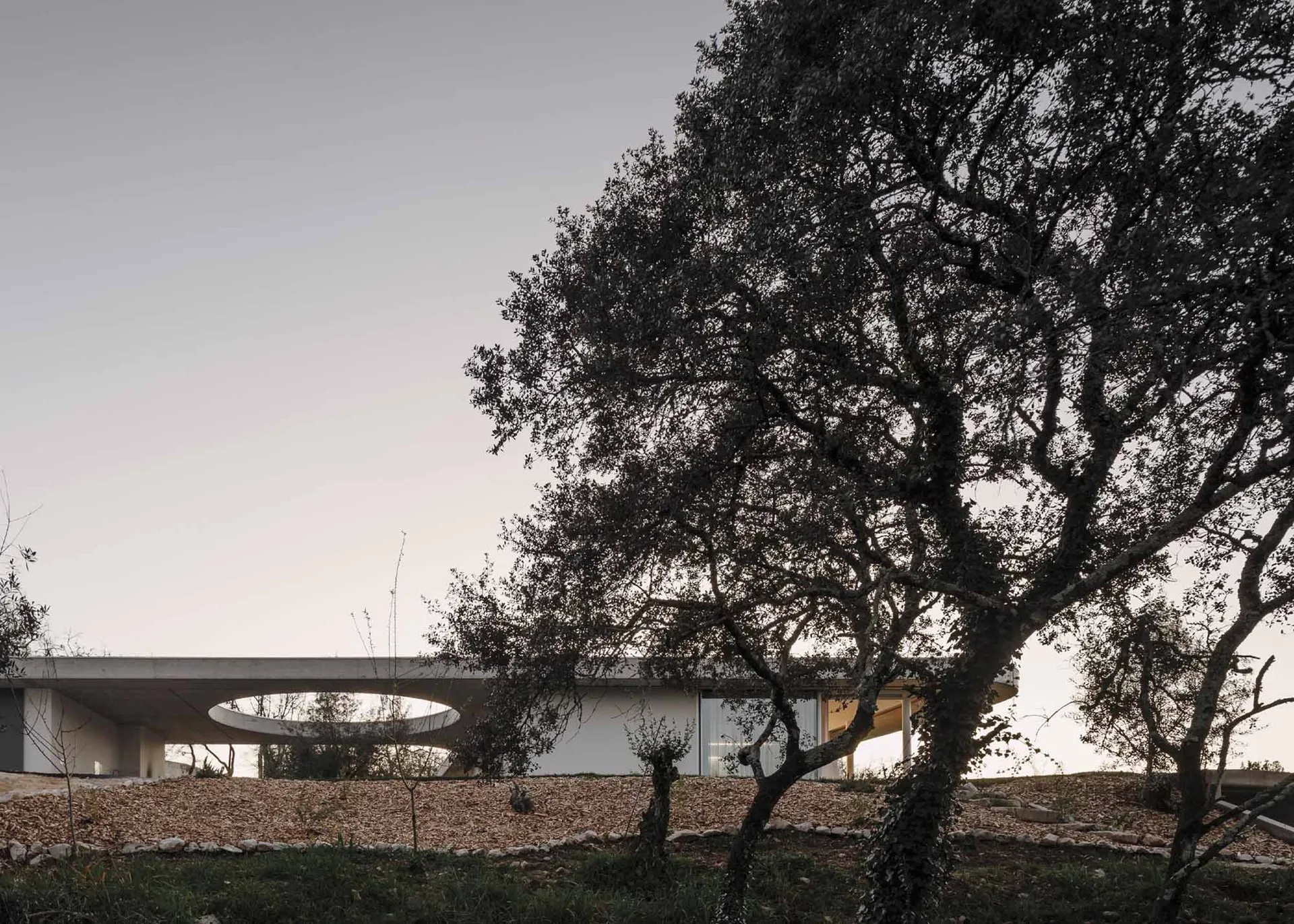 A modern, minimalist concrete house with a circular window and a natural landscape.