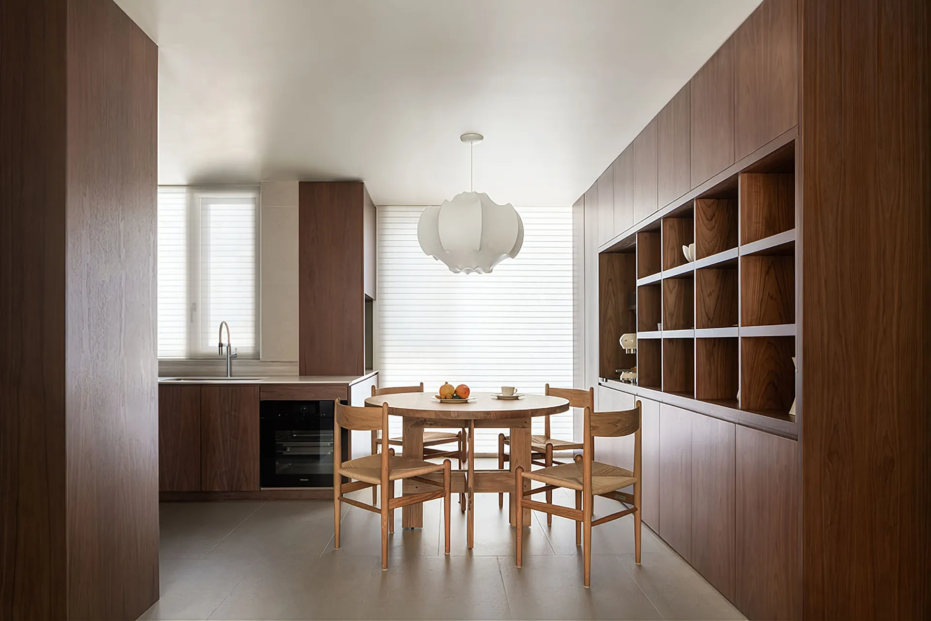 Modern residential kitchen featuring wooden furniture, a round dining table with chairs, and a large window with blinds.
