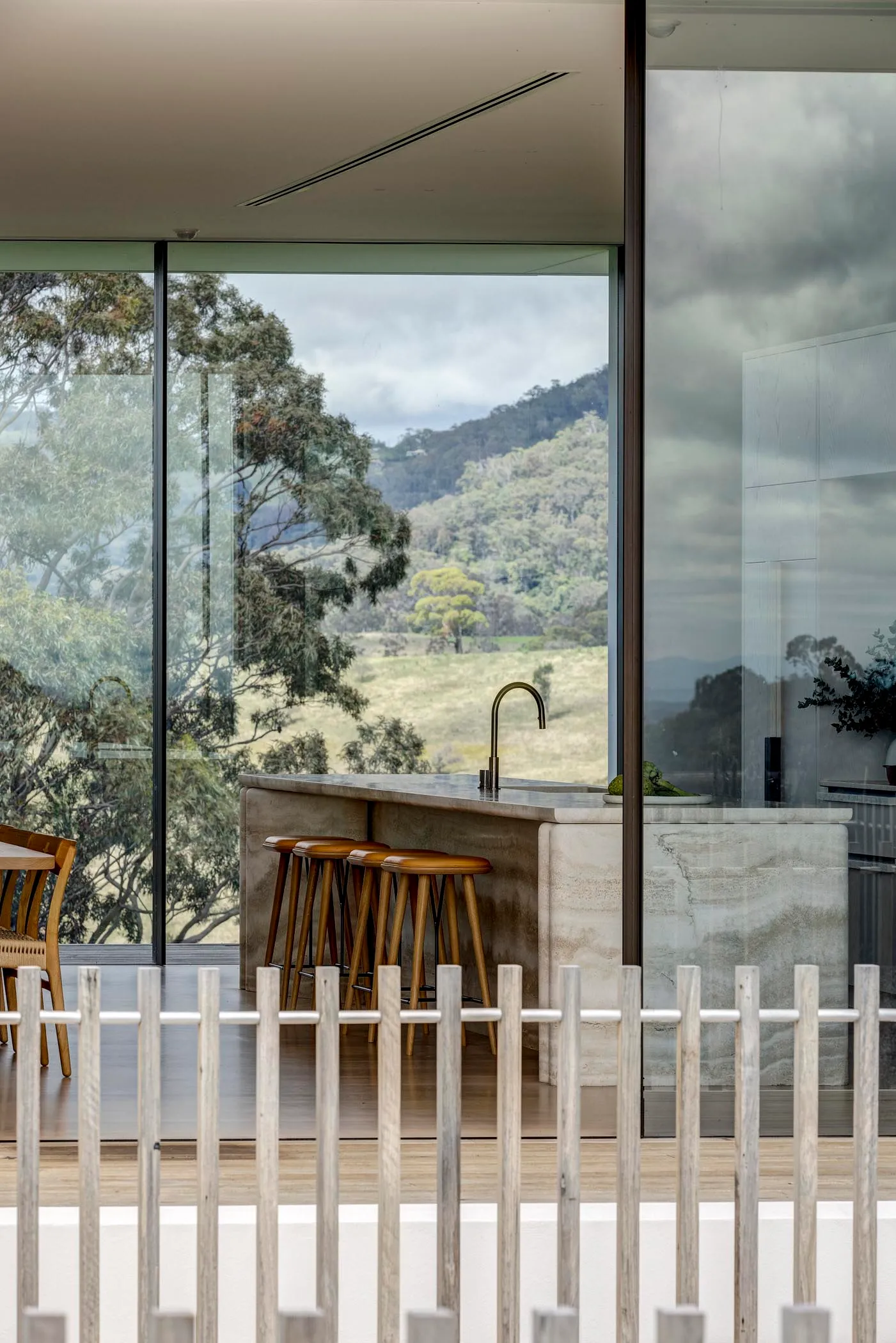 A modern minimalist kitchen with a concrete countertop and a view of lush green hills through large windows.