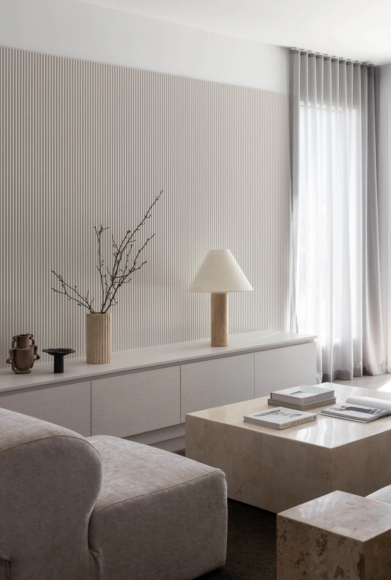 A modern minimalist living room with concrete furniture and a minimalist table lamp, featuring white curtains and a striped w