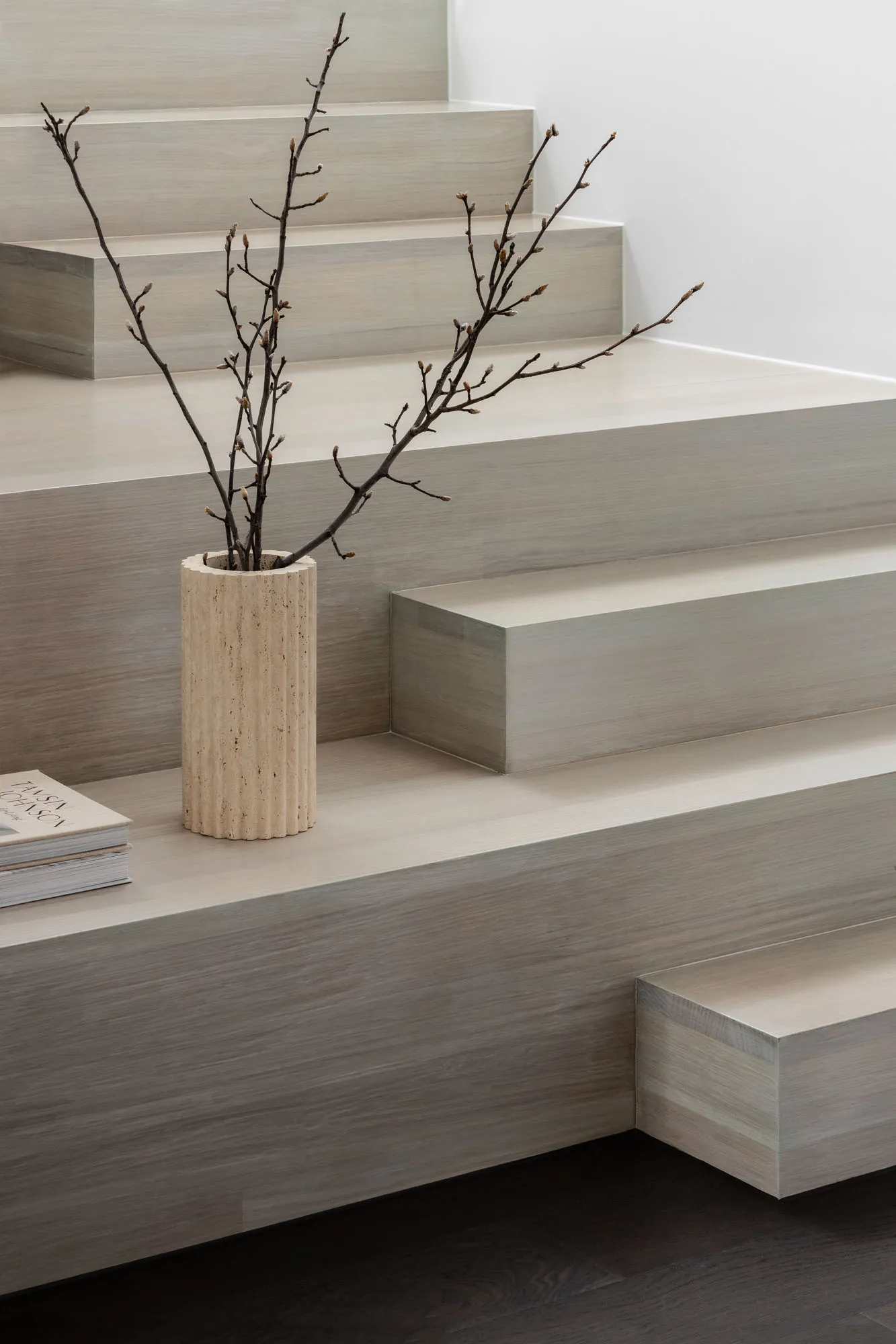 A minimalist interior featuring sleek, wooden stairs with a vase of twigs on the landing.