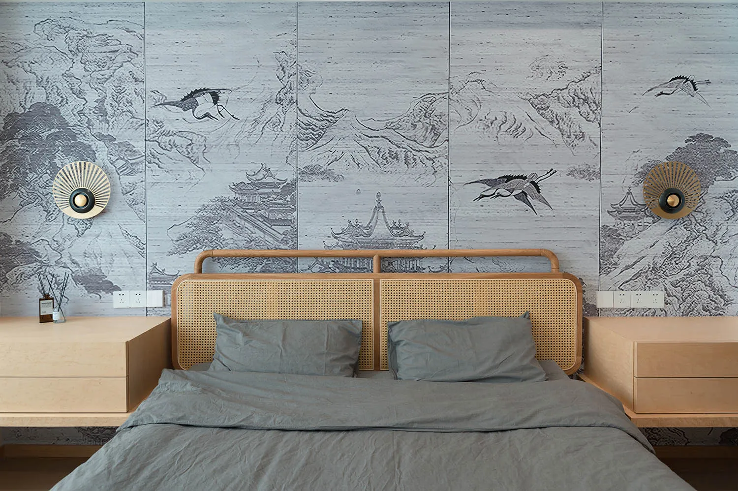 A bedroom with a bed featuring rattan headboard and gray bedding, against a wall with illustrated natural landscapes.