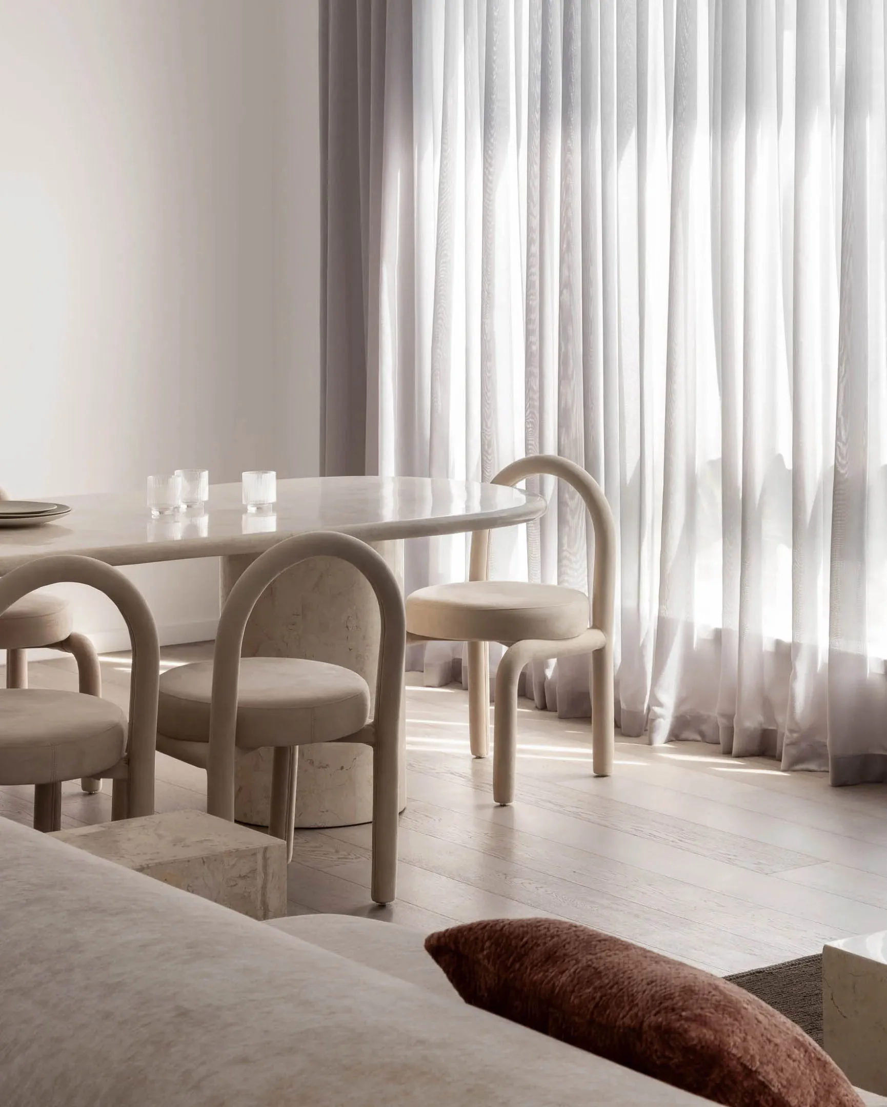Modern minimalist dining room featuring a sleek marble table, plush fabric chairs, and wooden flooring.