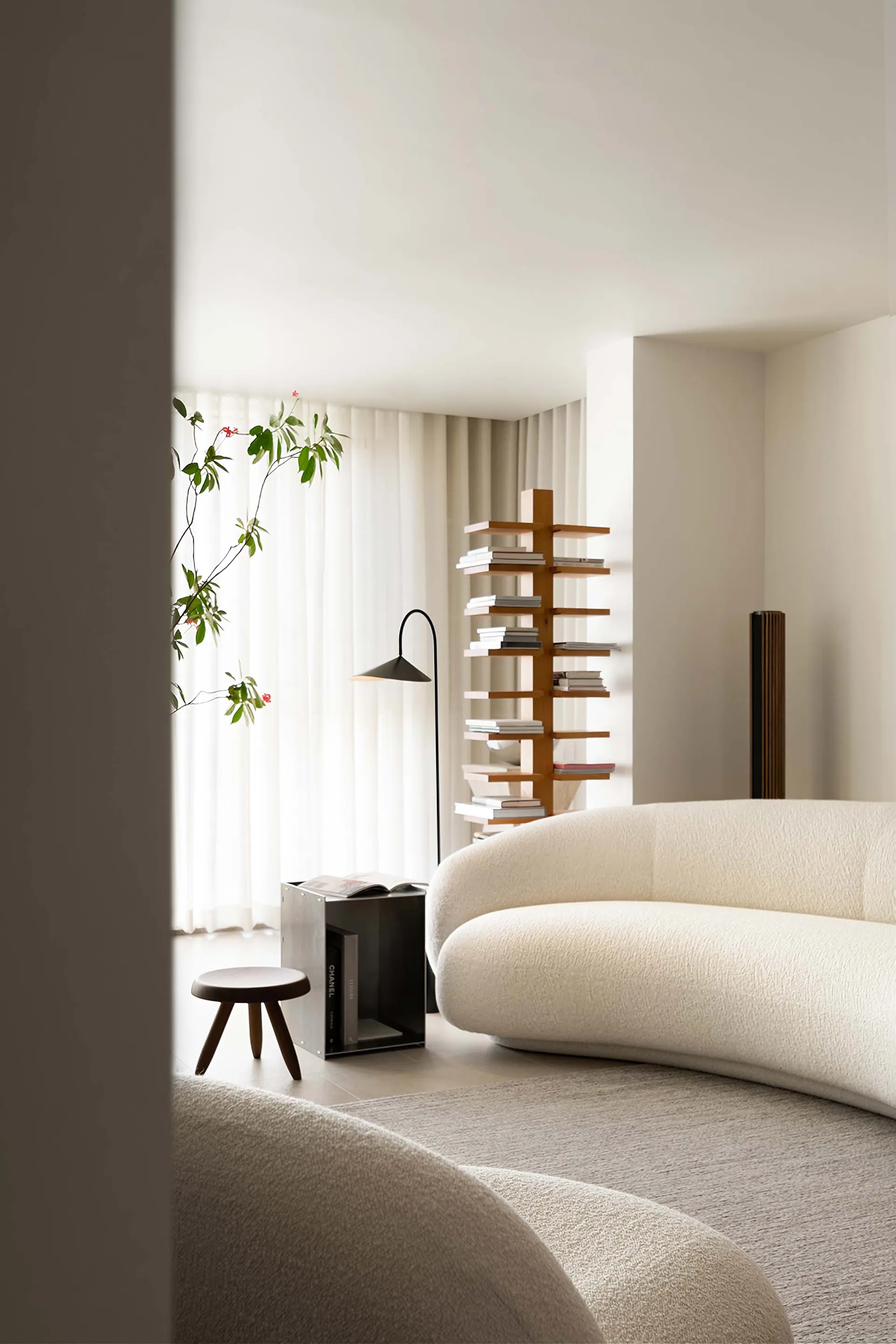 A modern minimalist living room with a white sofa, a tall bookshelf, and a floor lamp.
