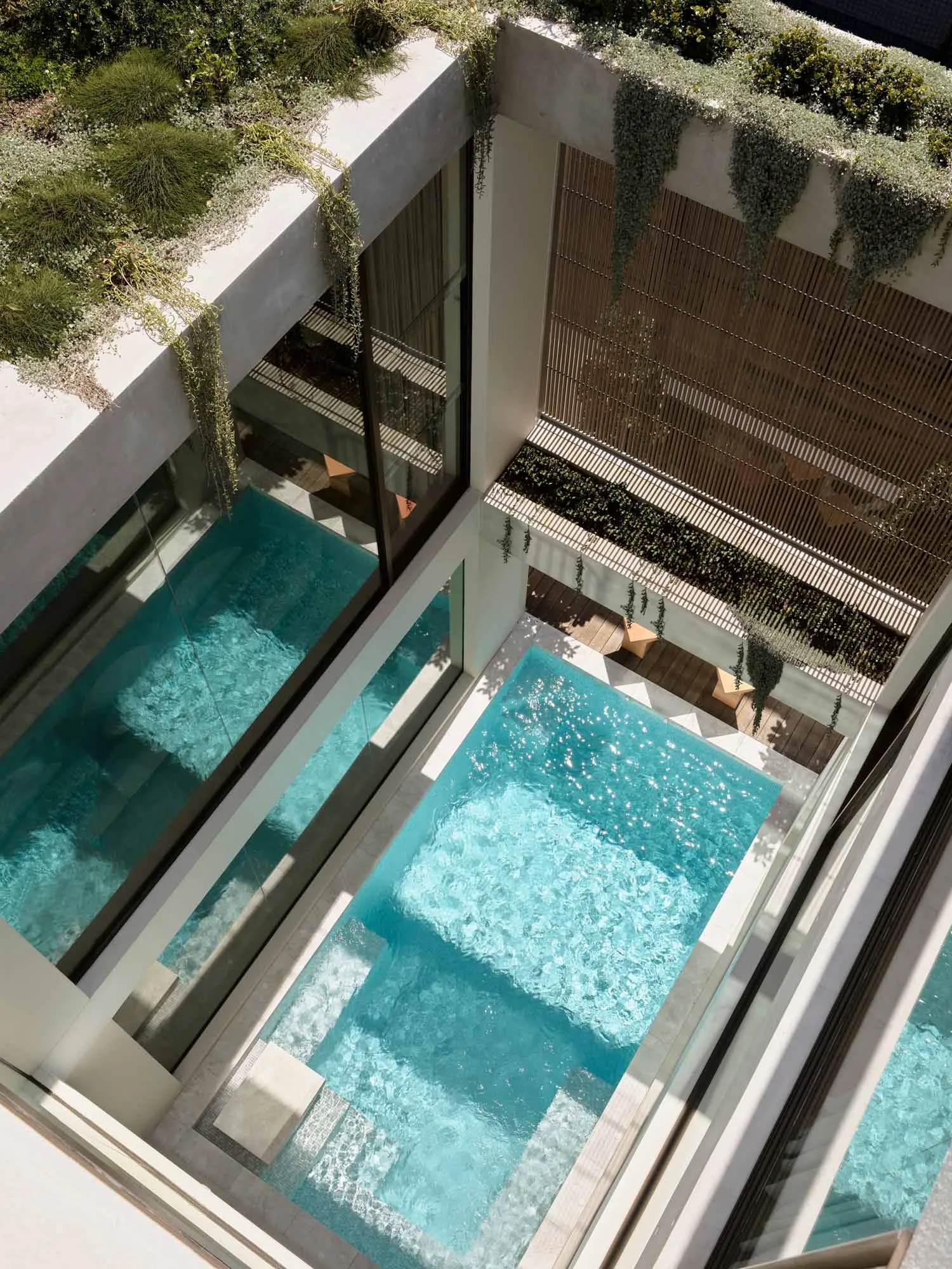 Modern residential pool area enclosed by concrete walls with glass panels.