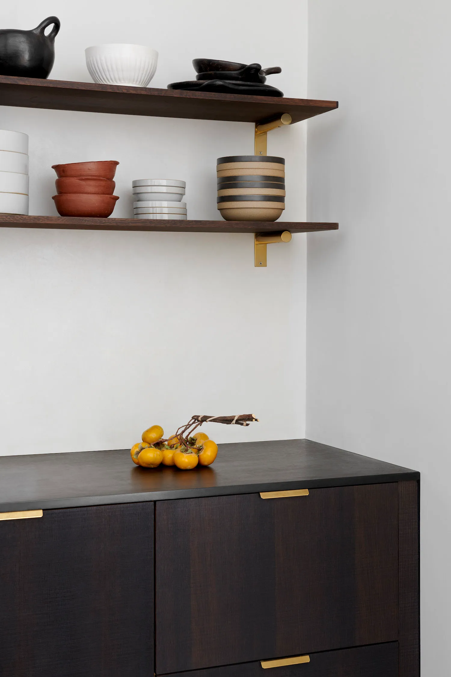 Modern storage cabinet with wooden finish and brass accents containing bowls and other items.