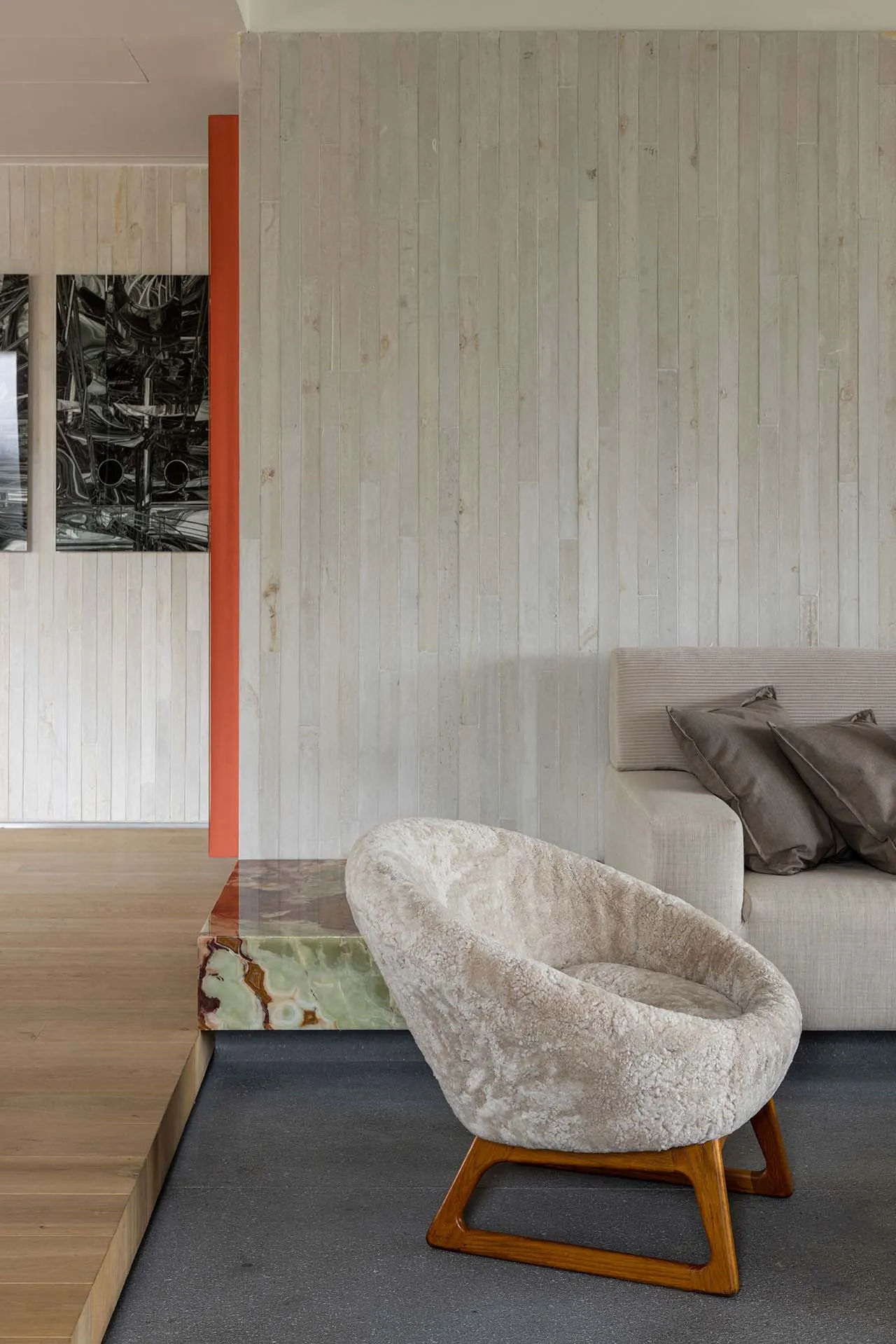 A modern living room with a concrete wall, wooden floors, a marble table, and upholstered seating.