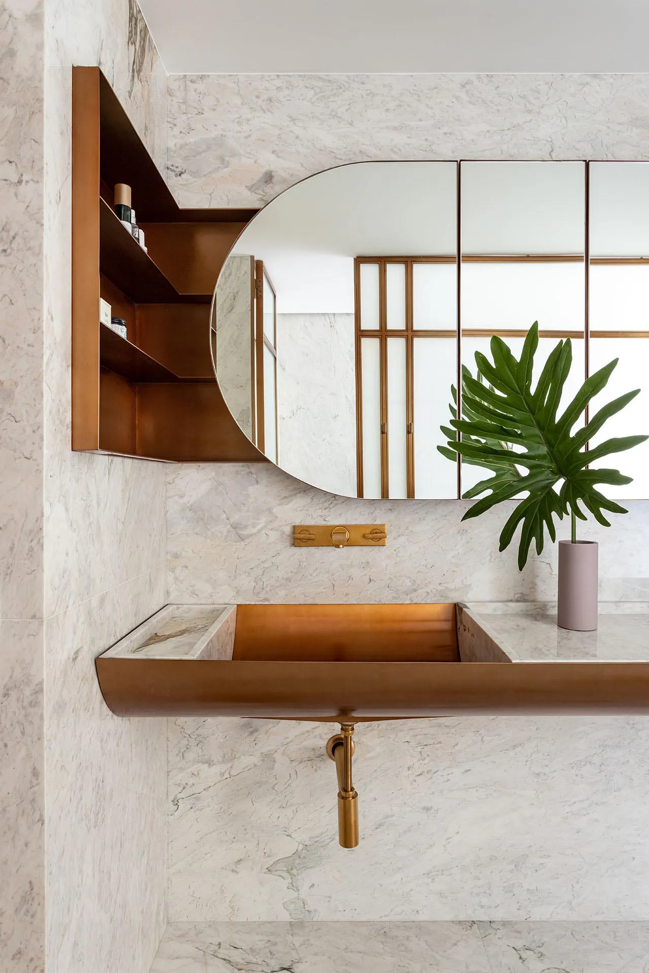 A modern bathroom with a marble sink and countertop, featuring a round mirror, open shelving, and a potted plant.