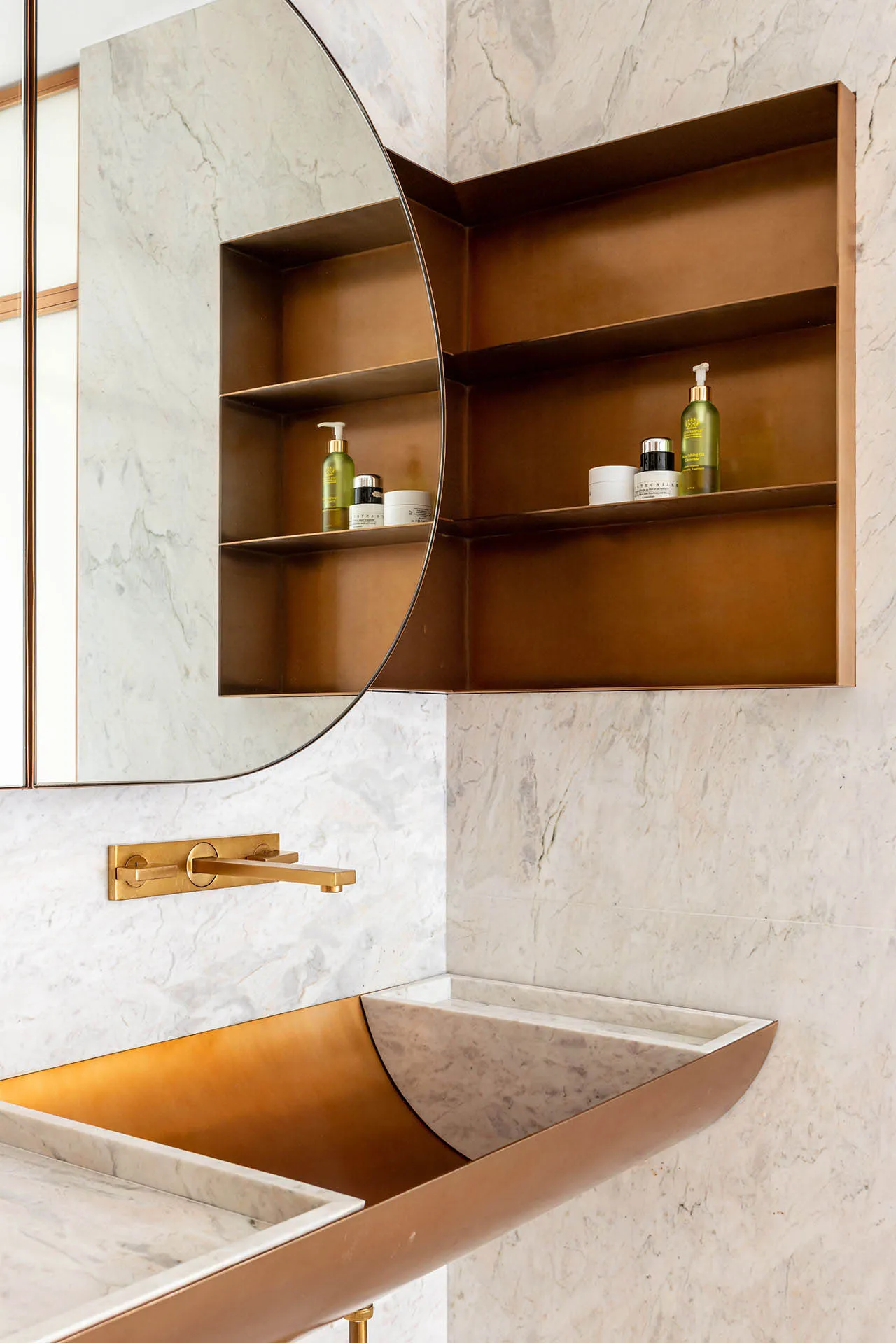 Modern bathroom featuring a marble and copper sink and floating shelf with beauty products.
