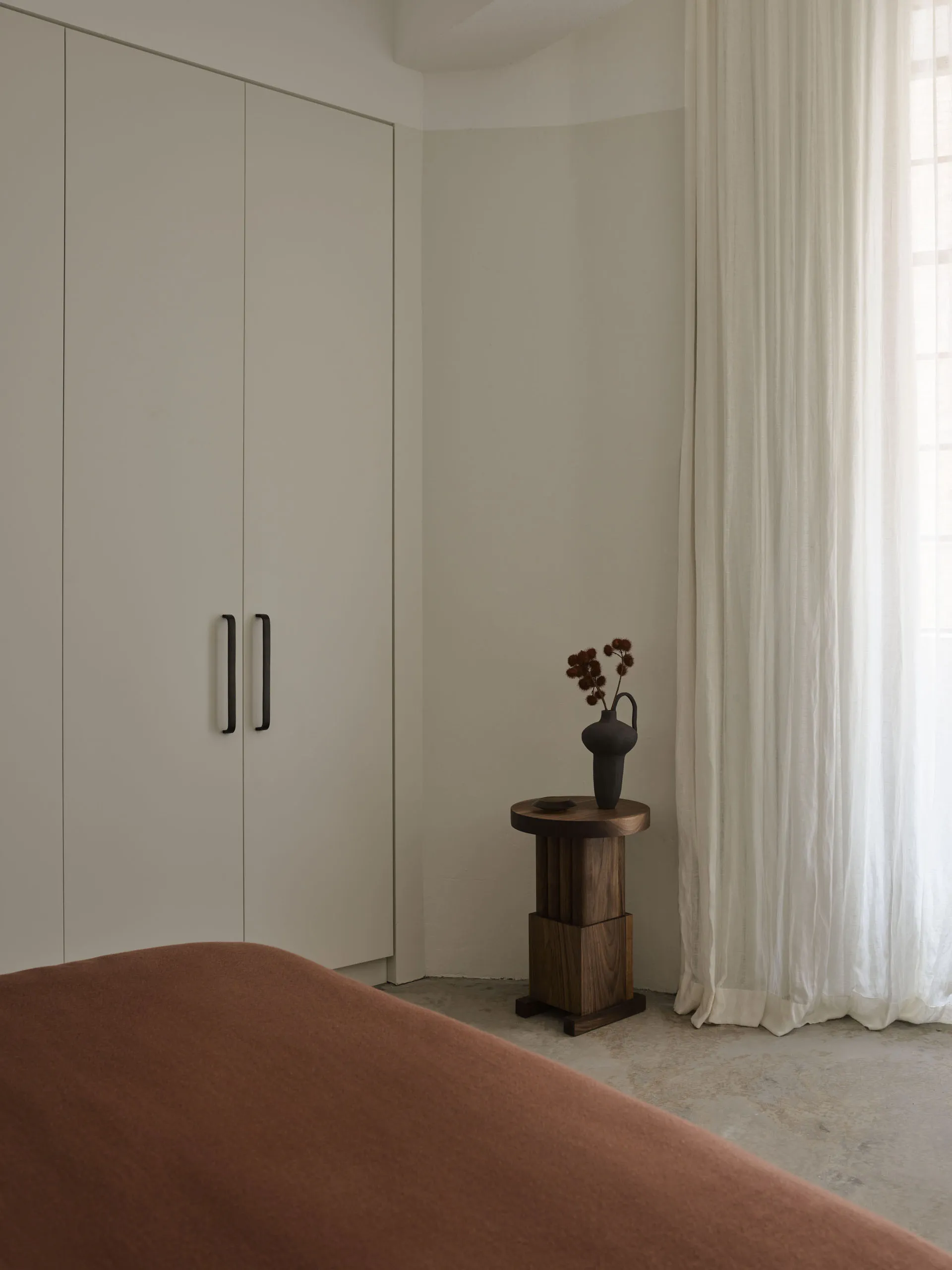 Minimalist bedroom featuring a textured bed, white curtains, and a white wardrobe with black handles.