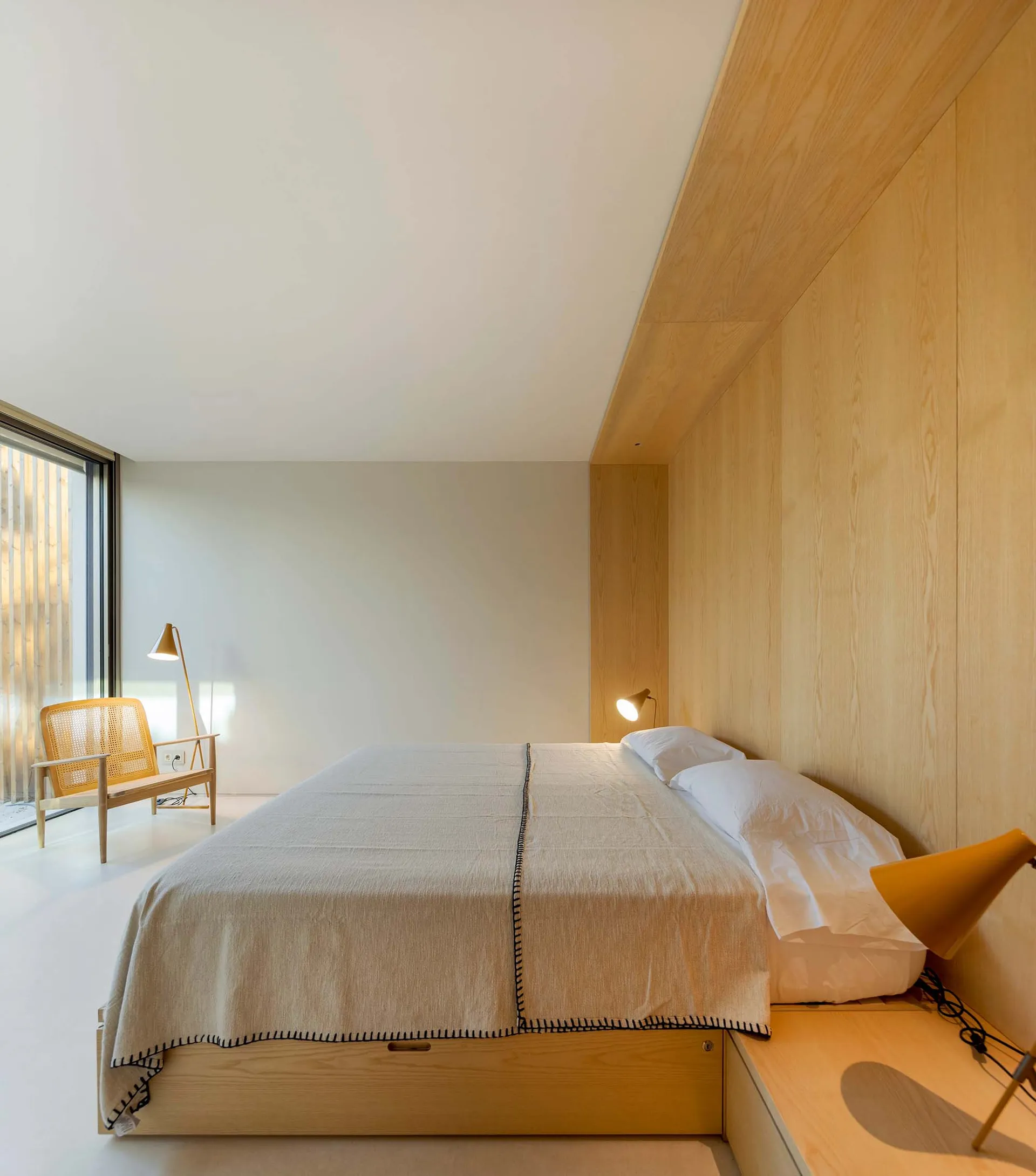 Modern minimalist bedroom with wooden walls and furniture, featuring a bed with a wooden headboard and matching bedside table