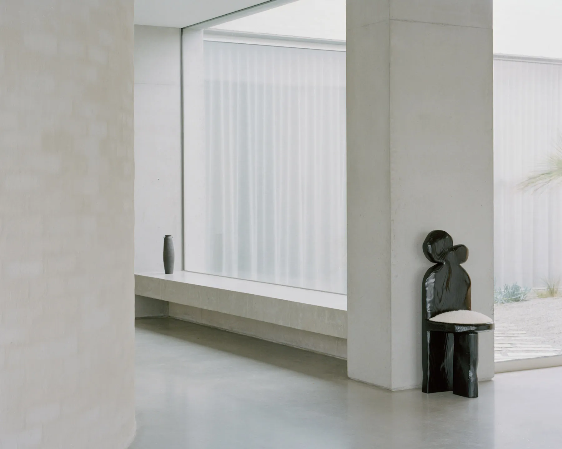 Modern minimalist interior design featuring concrete walls and floor, large frosted glass window, and a unique black chair wi
