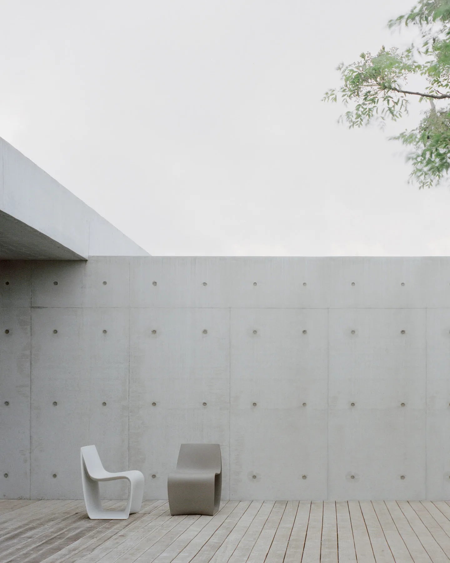 A minimalist outdoor space featuring a white and beige concrete wall and a wooden deck.
