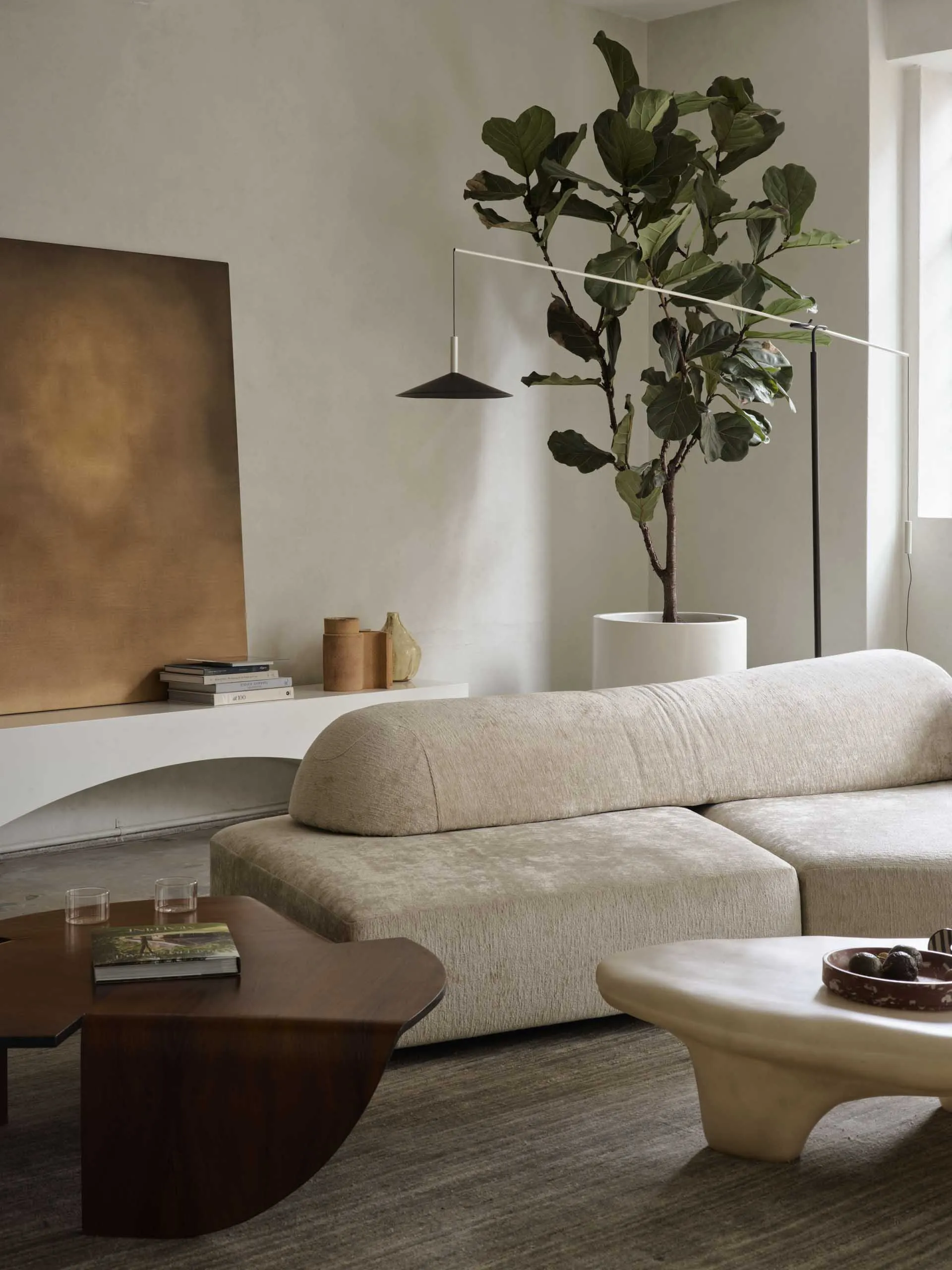 A stylish modern living room with beige furniture, a potted plant, and a coffee table with books and decorative items.