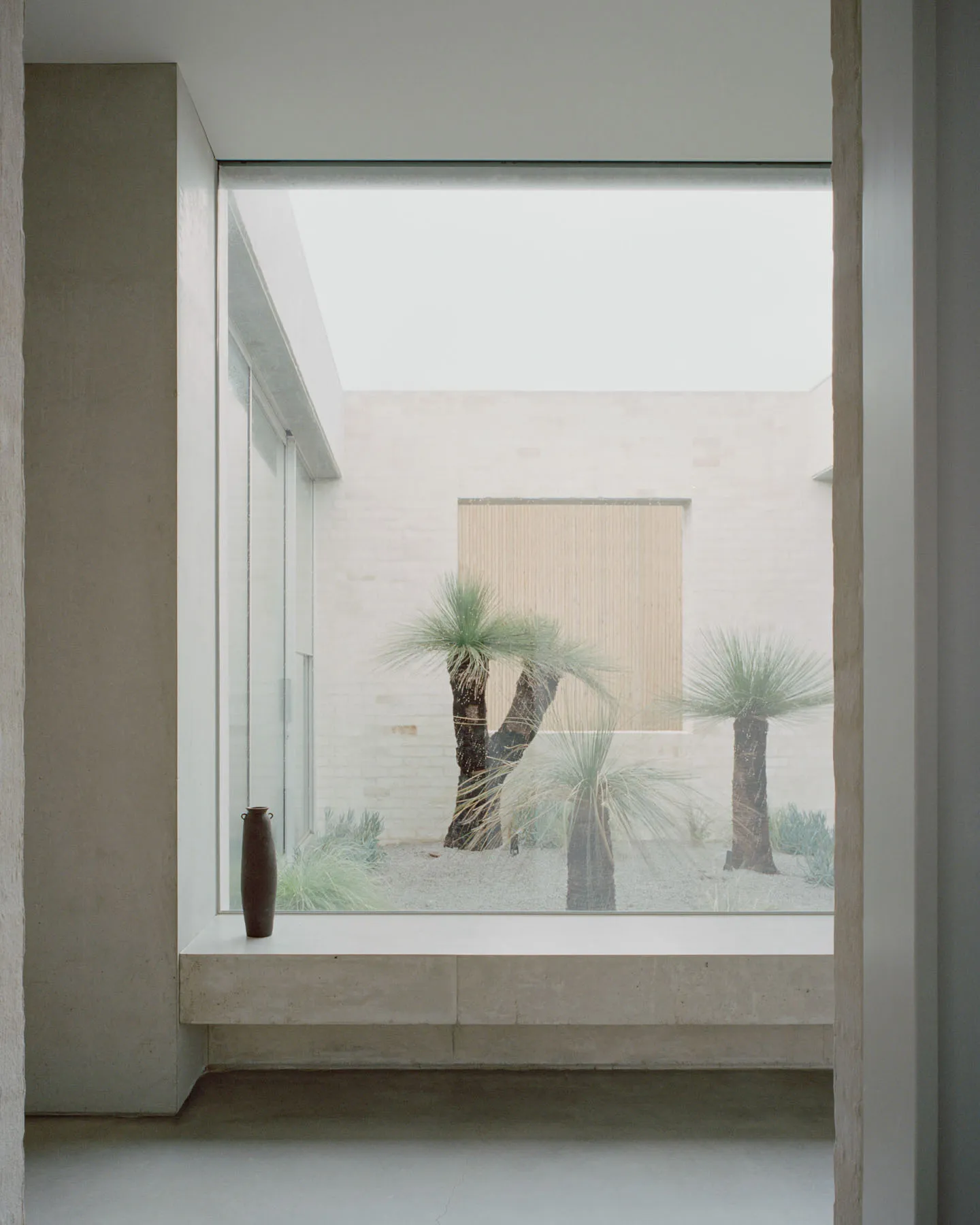 A minimalist living space with a large window showcasing a serene courtyard with palm trees.