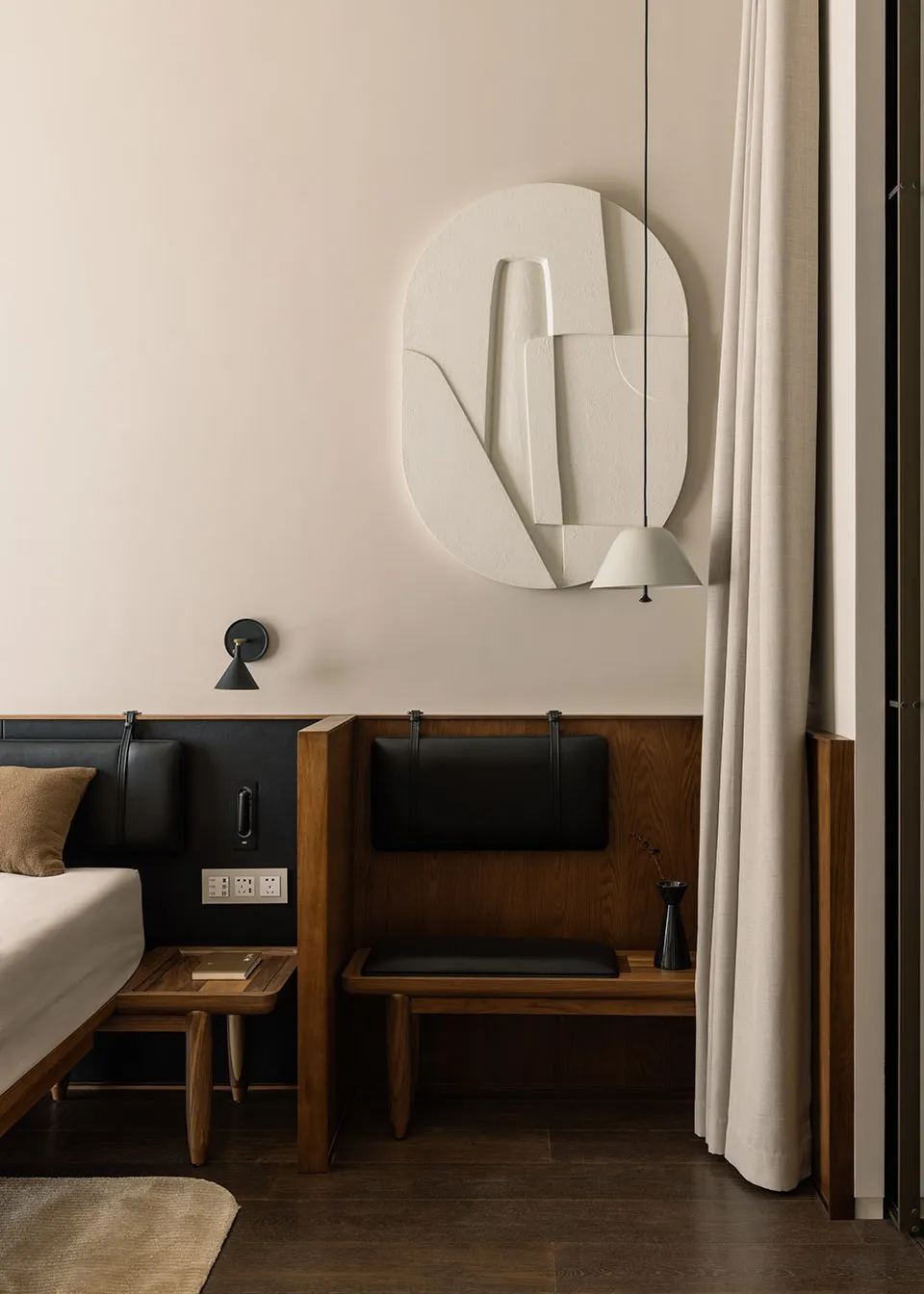 A modern bedroom with wooden furniture, a white relief sculpture on the wall, and a hanging lamp.
