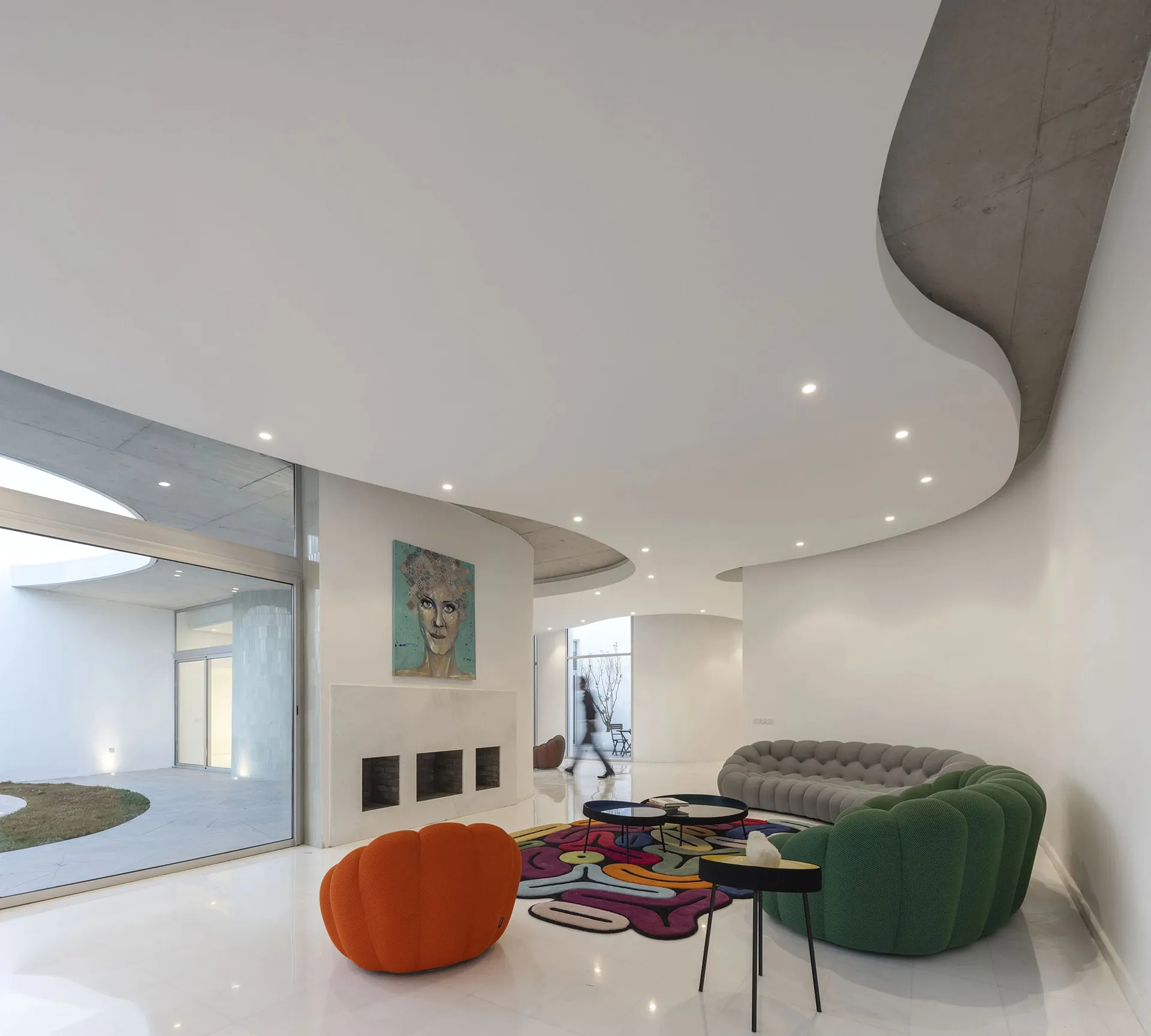 A modern living room with white concrete walls, colorful sofas and an abstract carpet.