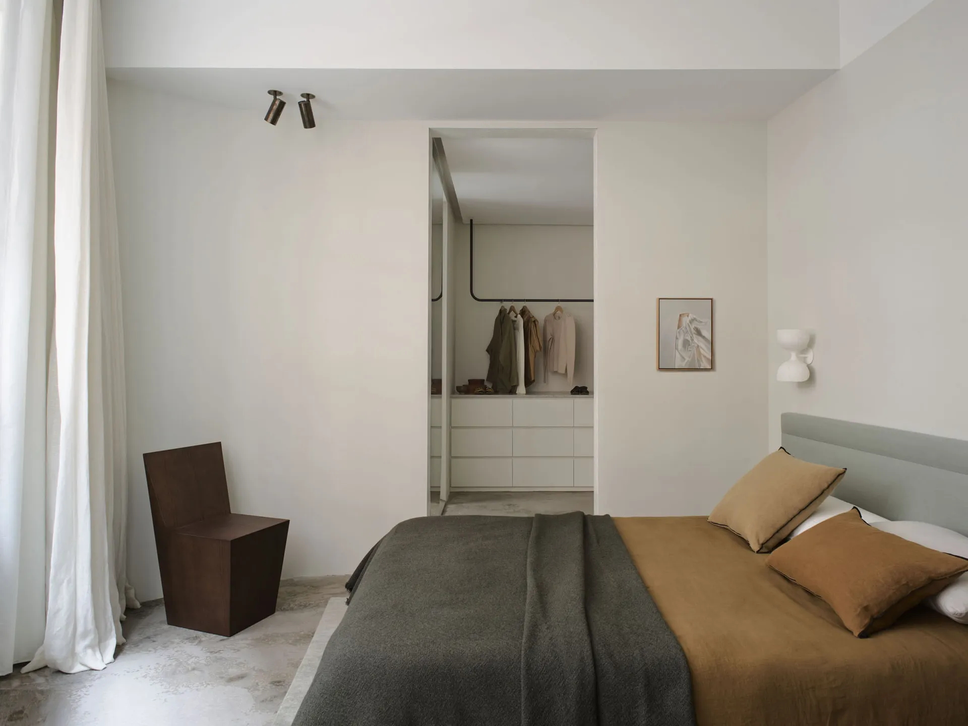 A minimalist bedroom featuring a minimalist wooden chair, concrete flooring, a bed with fabric bedding, and an open closet wi