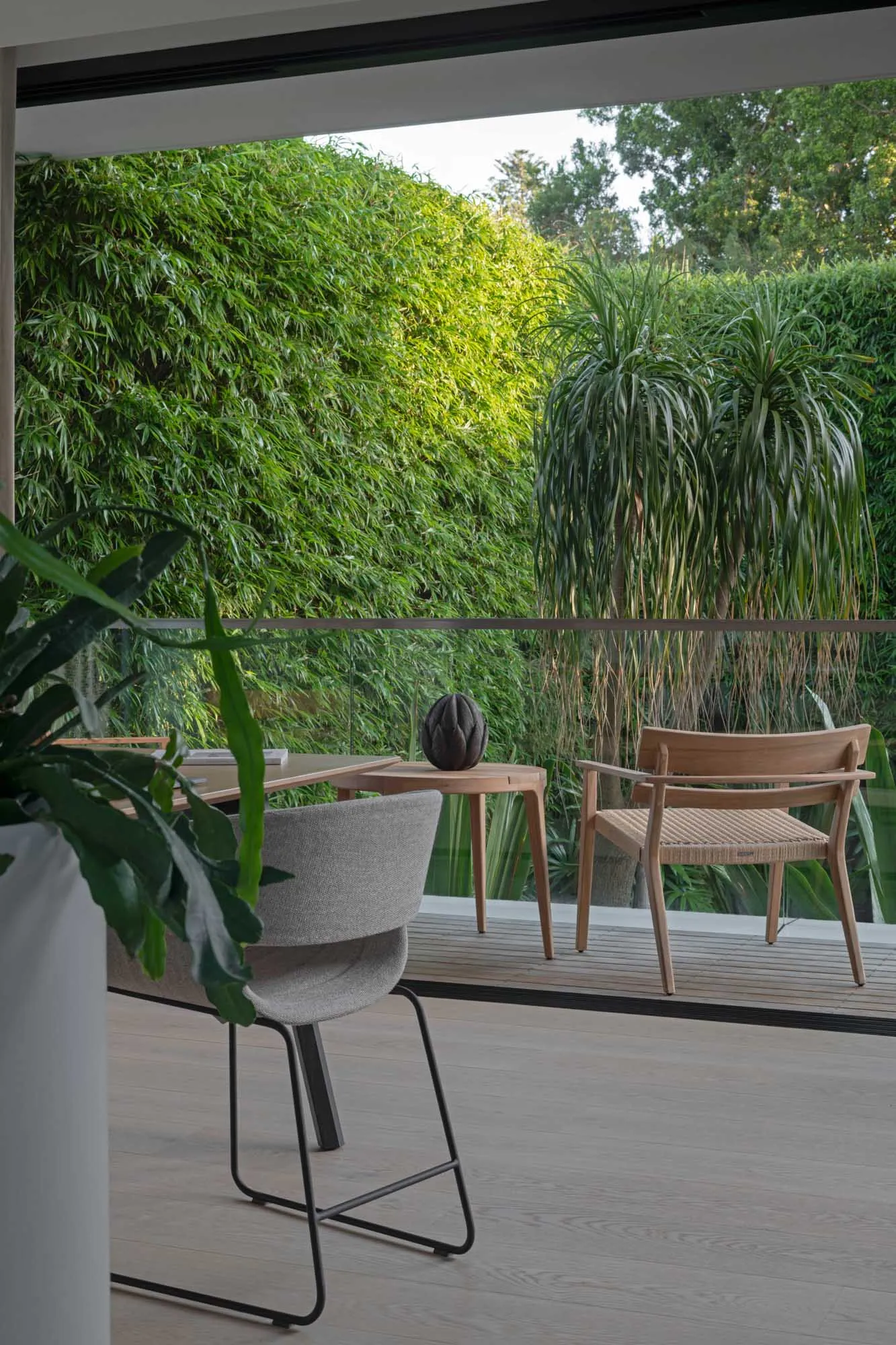 Modern interior patio area featuring wooden furniture and textile accents with lush greenery outside.