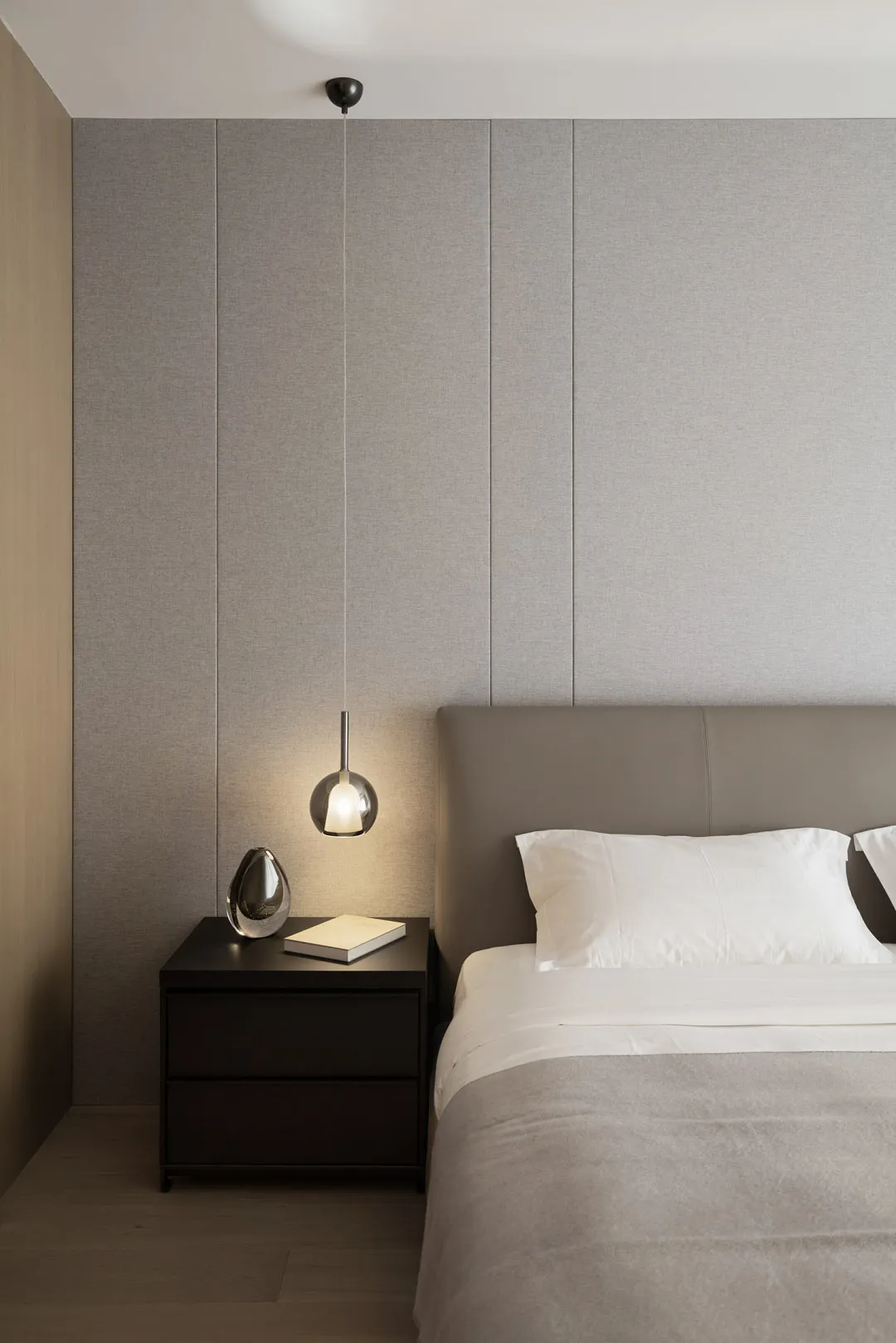 A minimalist bedroom featuring a fabric-covered bed, a sleek nightstand, and modern lighting.