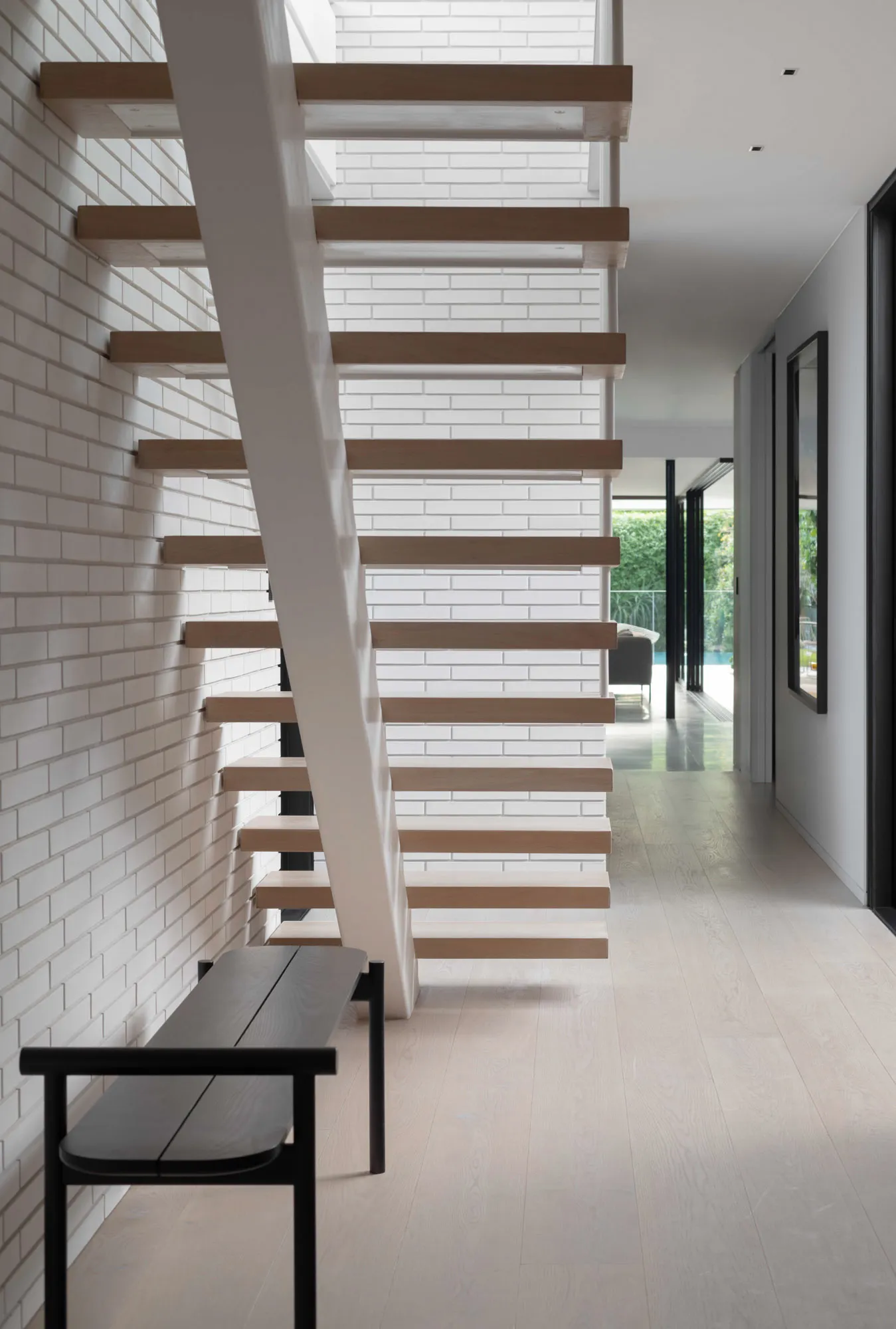 Modern floating staircase made of wood with a white brick wall and white flooring.