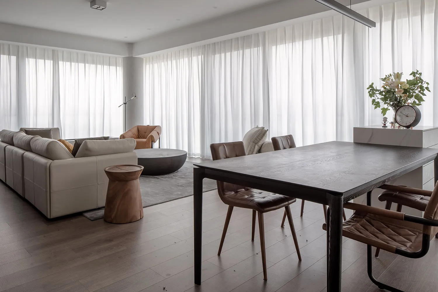 Modern industrial living room with wooden furniture and leather accents, featuring a large sofa, chairs, and a dining table.