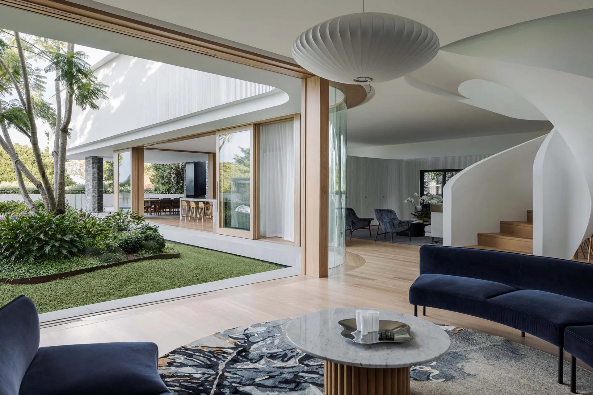 A modern living room featuring marble surfaces and wooden elements, glass walls, and a circular pendant light.