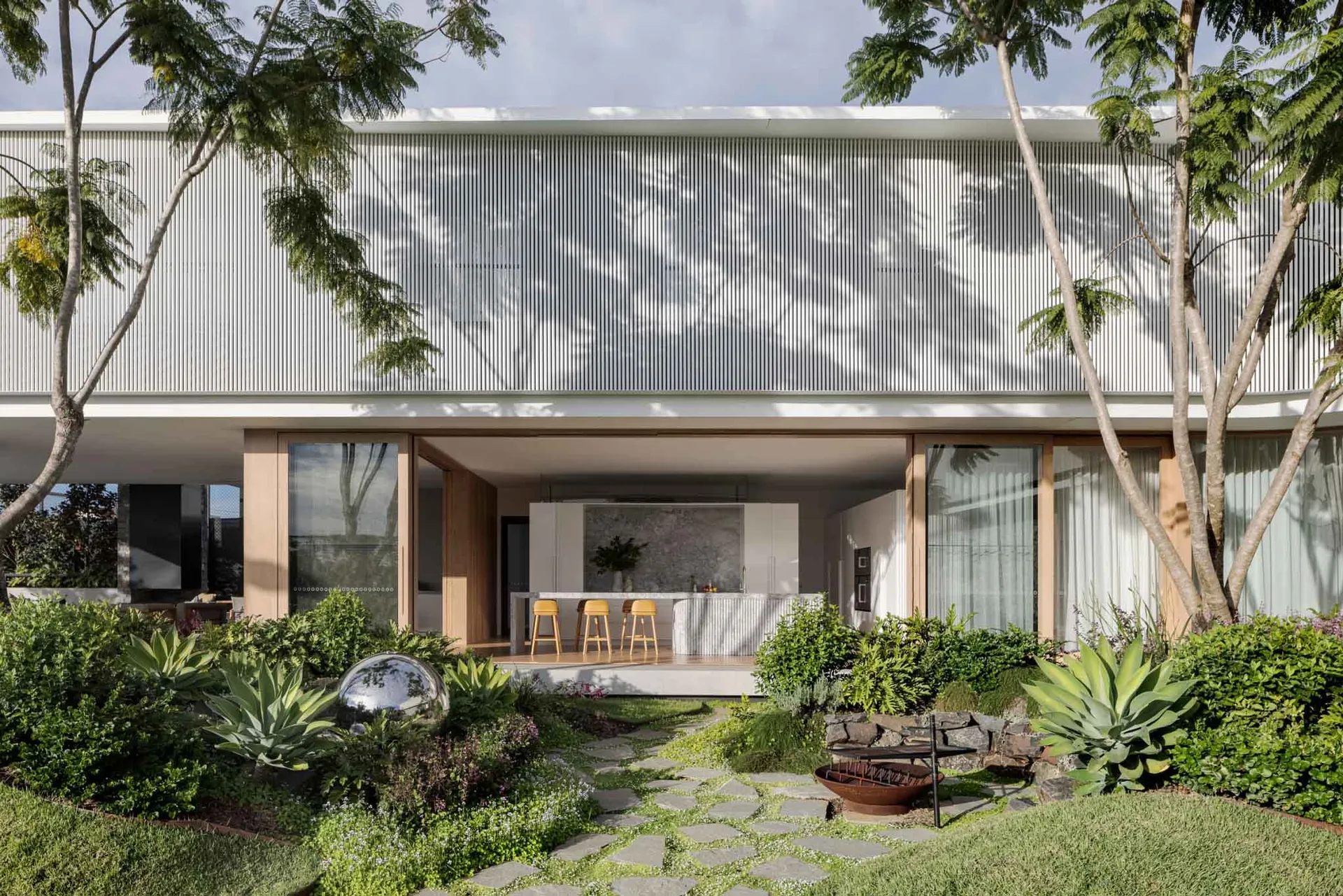A modern residential exterior featuring a metal-clad facade with large windows and a landscaped garden.