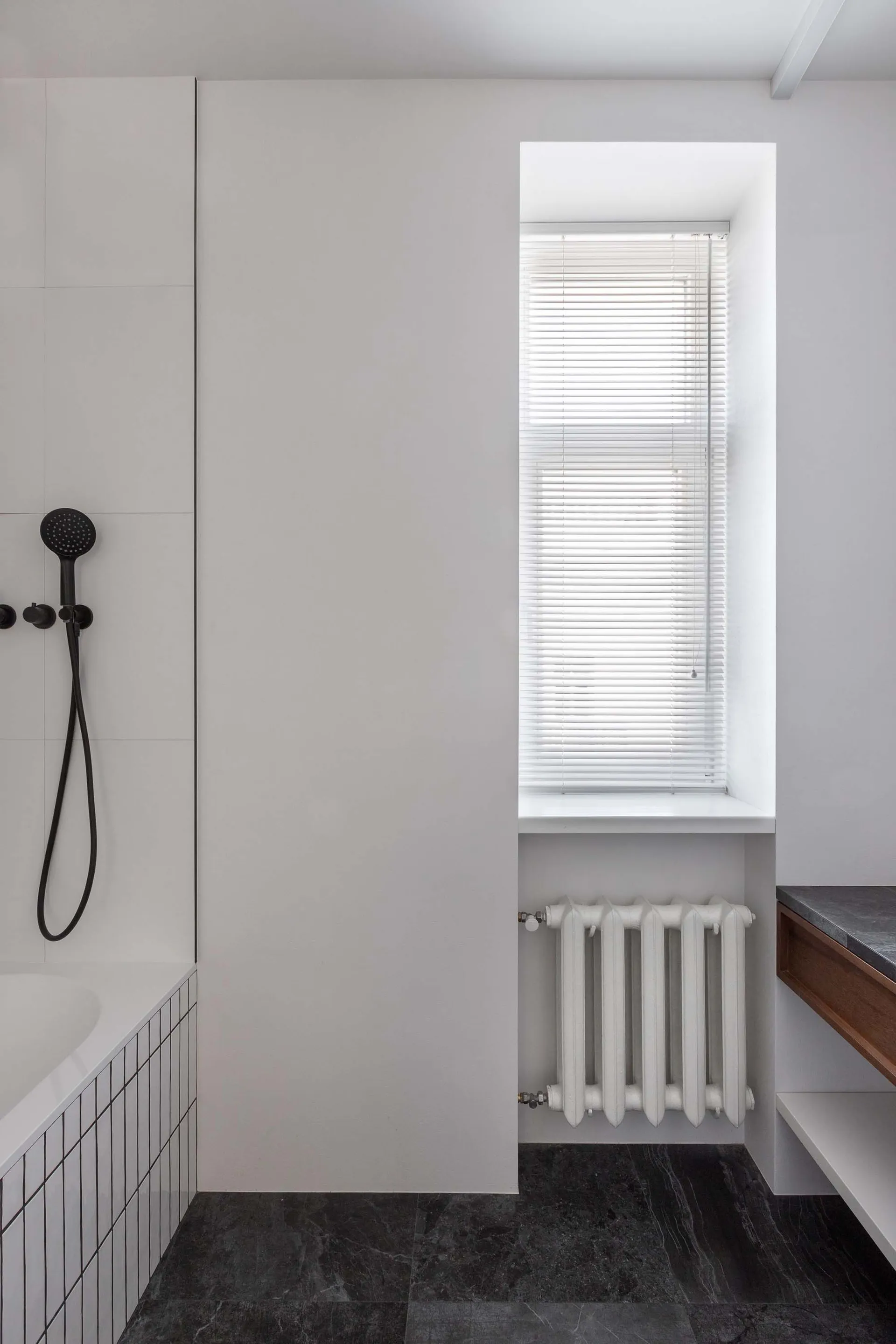 A modern minimalist bathroom with concrete elements, a window with blinds, and a radiator below it.