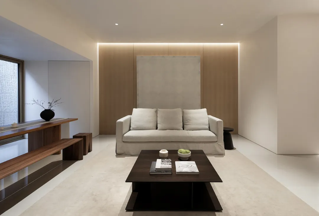 Modern minimalist living room with a white sofa, dark coffee table, and wooden accents.