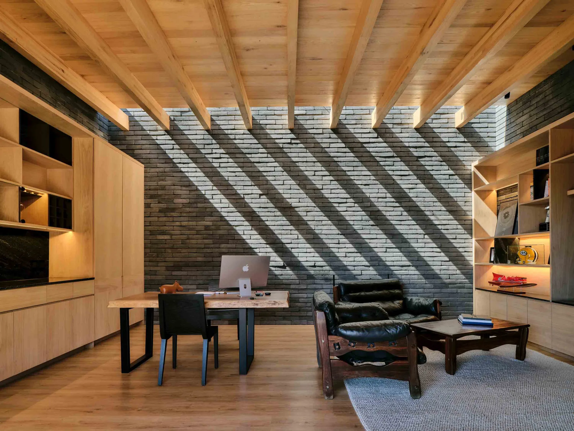 Industrial-style office space featuring a wooden ceiling and brick accent wall with sunlight streaming through