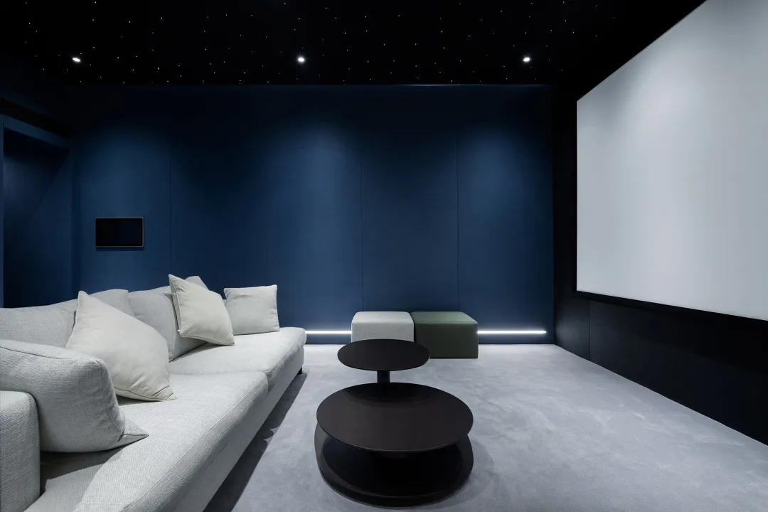 Modern minimalist living room featuring a white sofa with white cushions, a dark round coffee table, and dark blue walls with