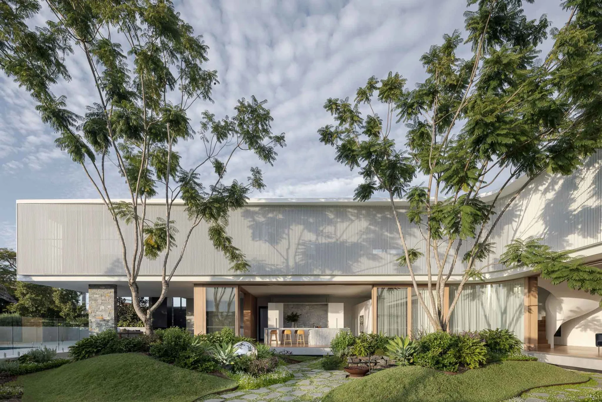A contemporary exterior house with large glass windows and greenery surrounding it.