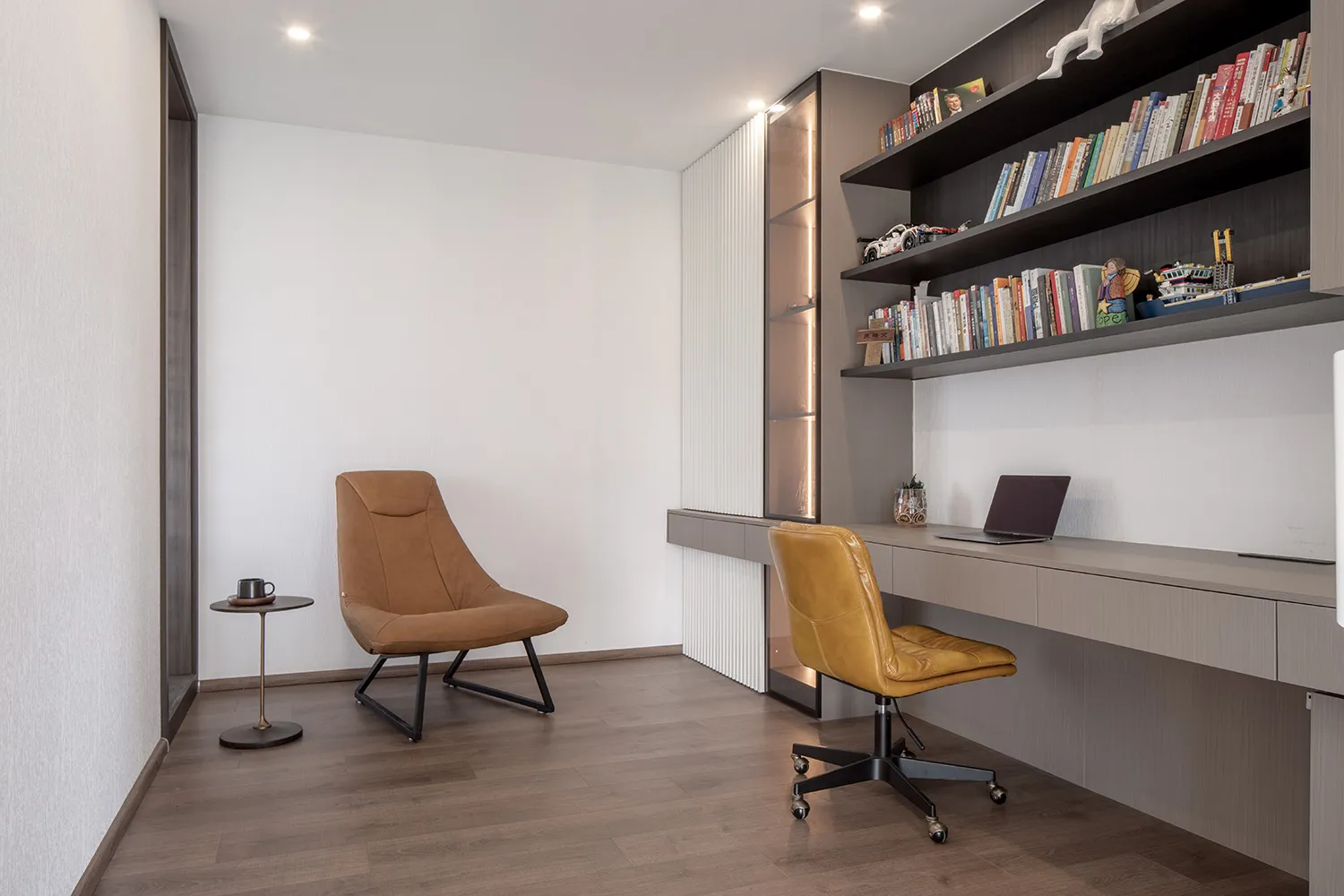 A modern home office with a wooden floor, brown leather chairs, and a built-in bookshelf.