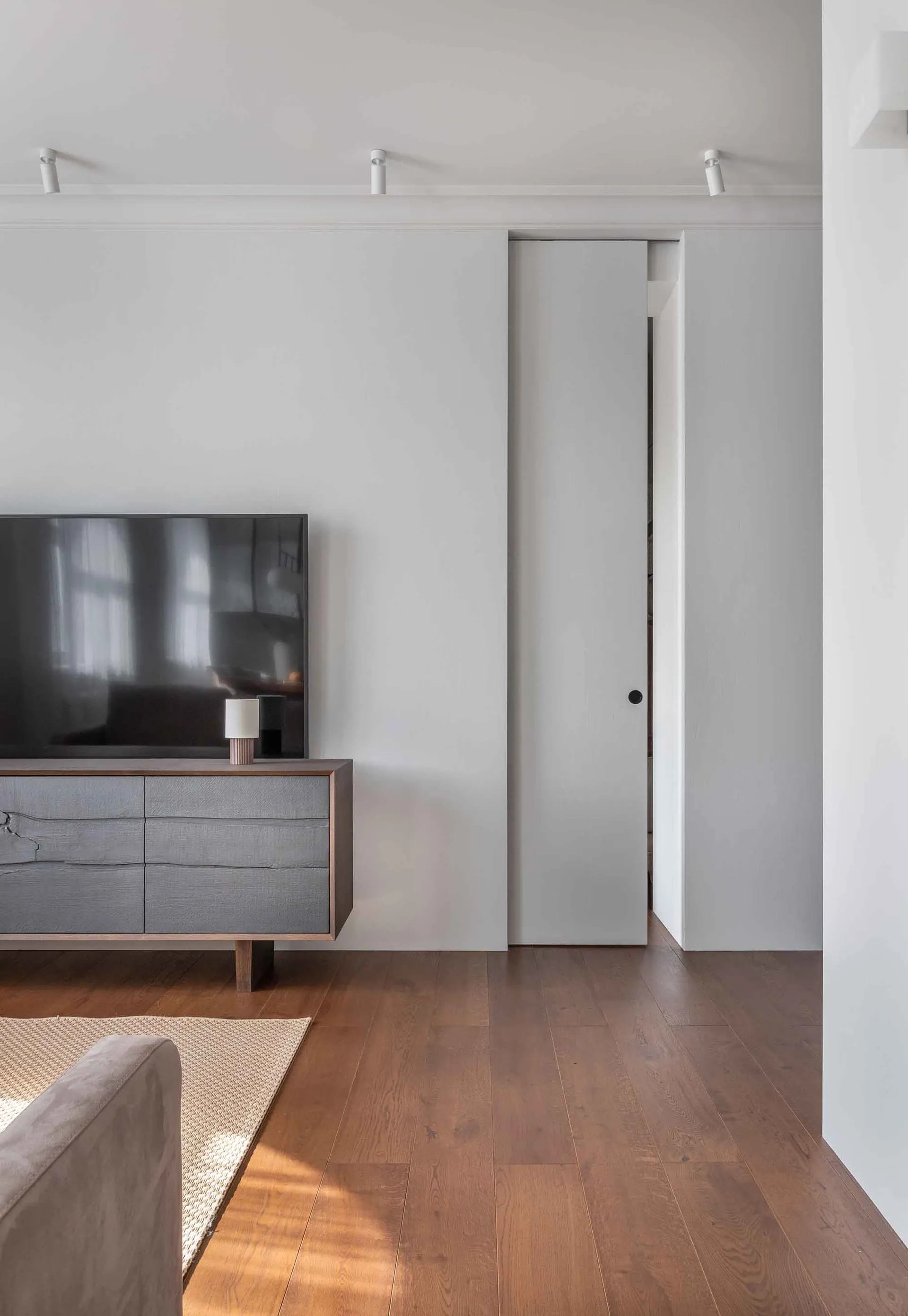 Modern, minimalist living room featuring sleek lines, wood flooring, a sliding door, and minimal furniture.