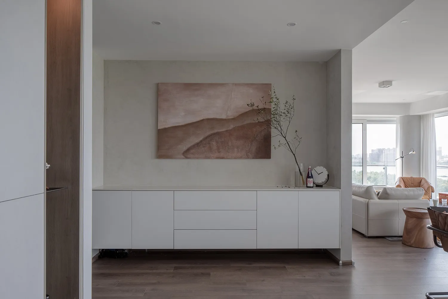 A modern living room with white furniture and a plant in a vase on a sideboard.