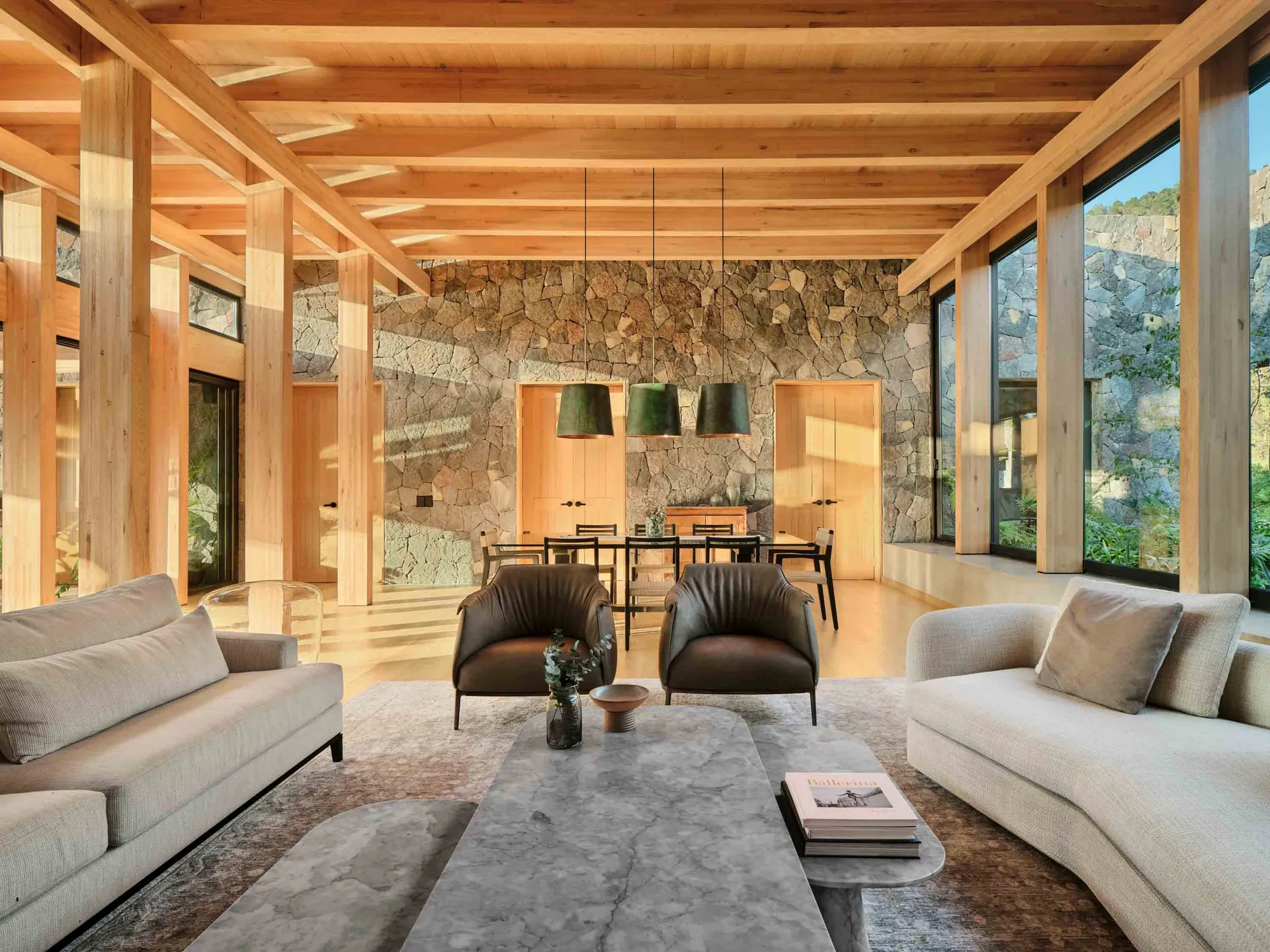A modern living room featuring wooden beams, a stone accent wall, and white sofas.