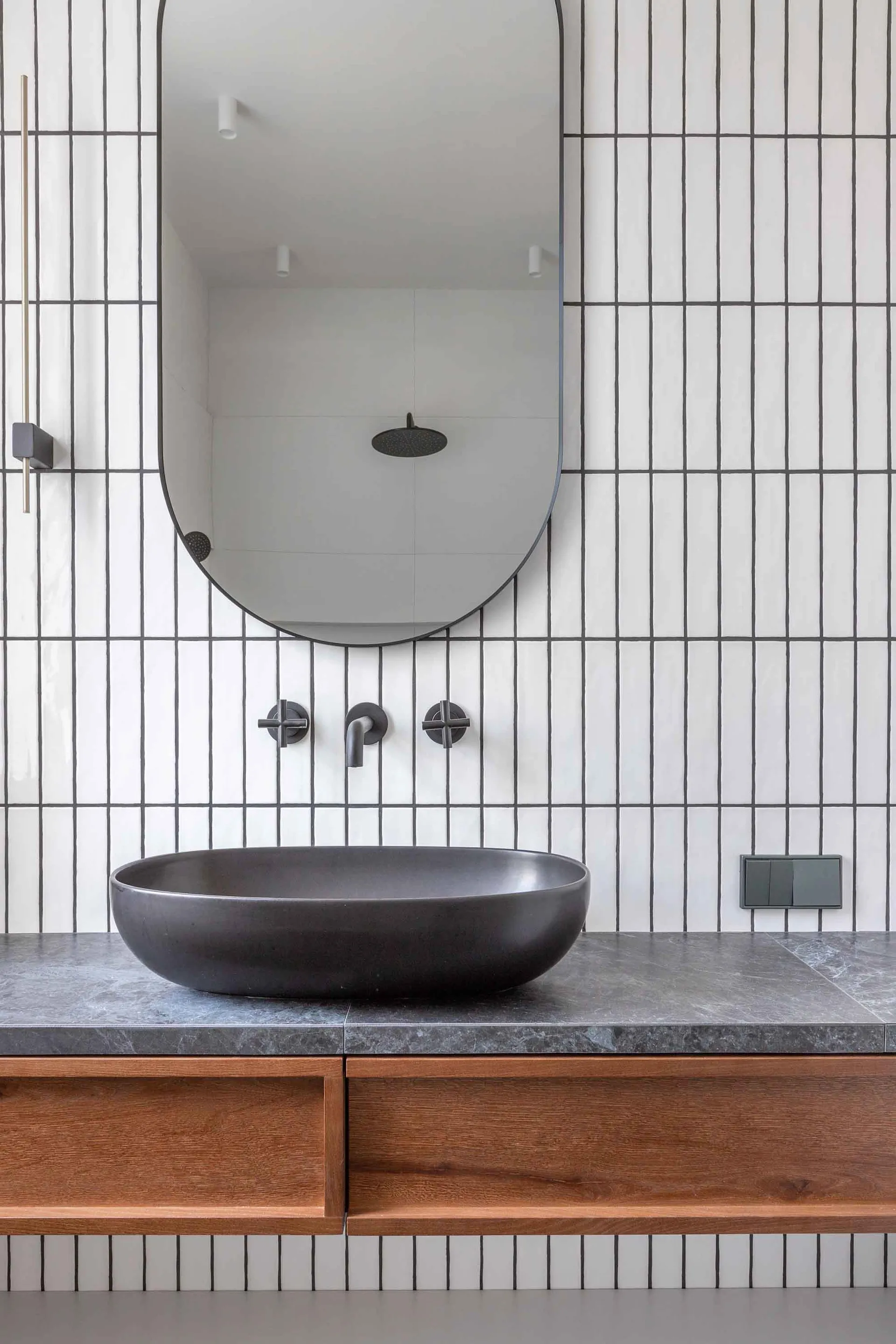 Modern minimalist bathroom with a black concrete sink, wooden vanity, and ceramic tiles with vertical lines.