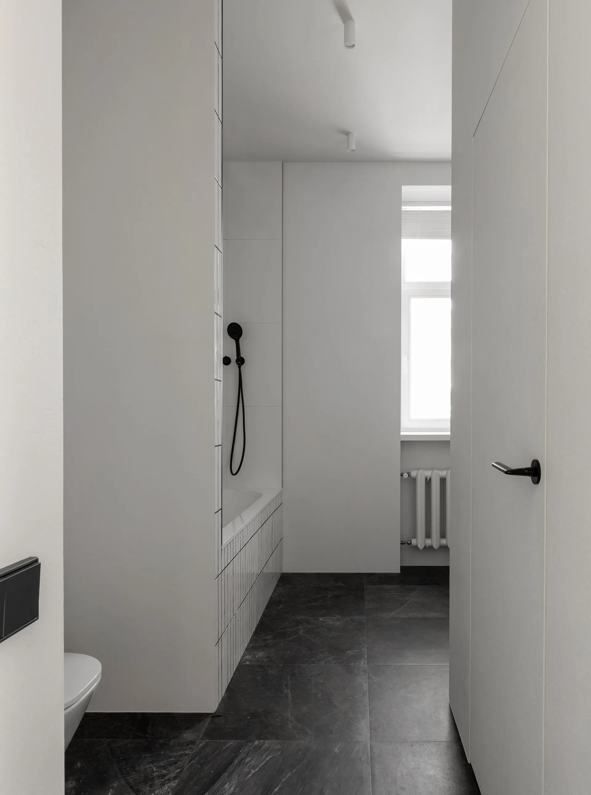 Modern minimalist white bathroom with black marble flooring and white tiled shower area.