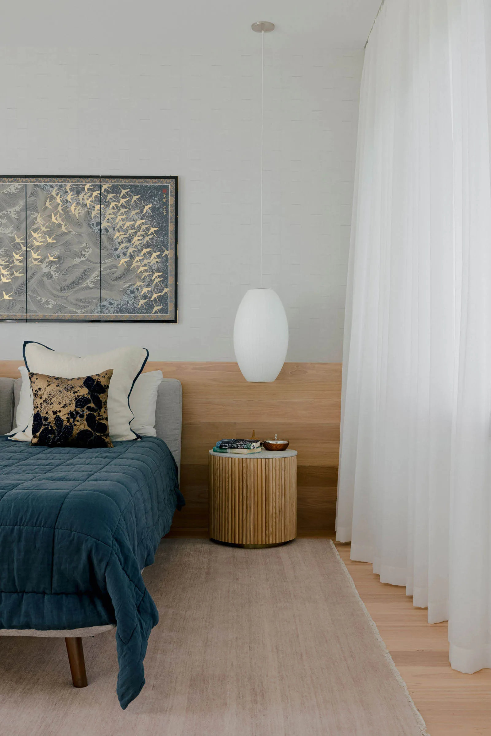 A minimalist bedroom featuring a bed with cotton linens and wood headboard, alongside a glass bedside table with a pendant la