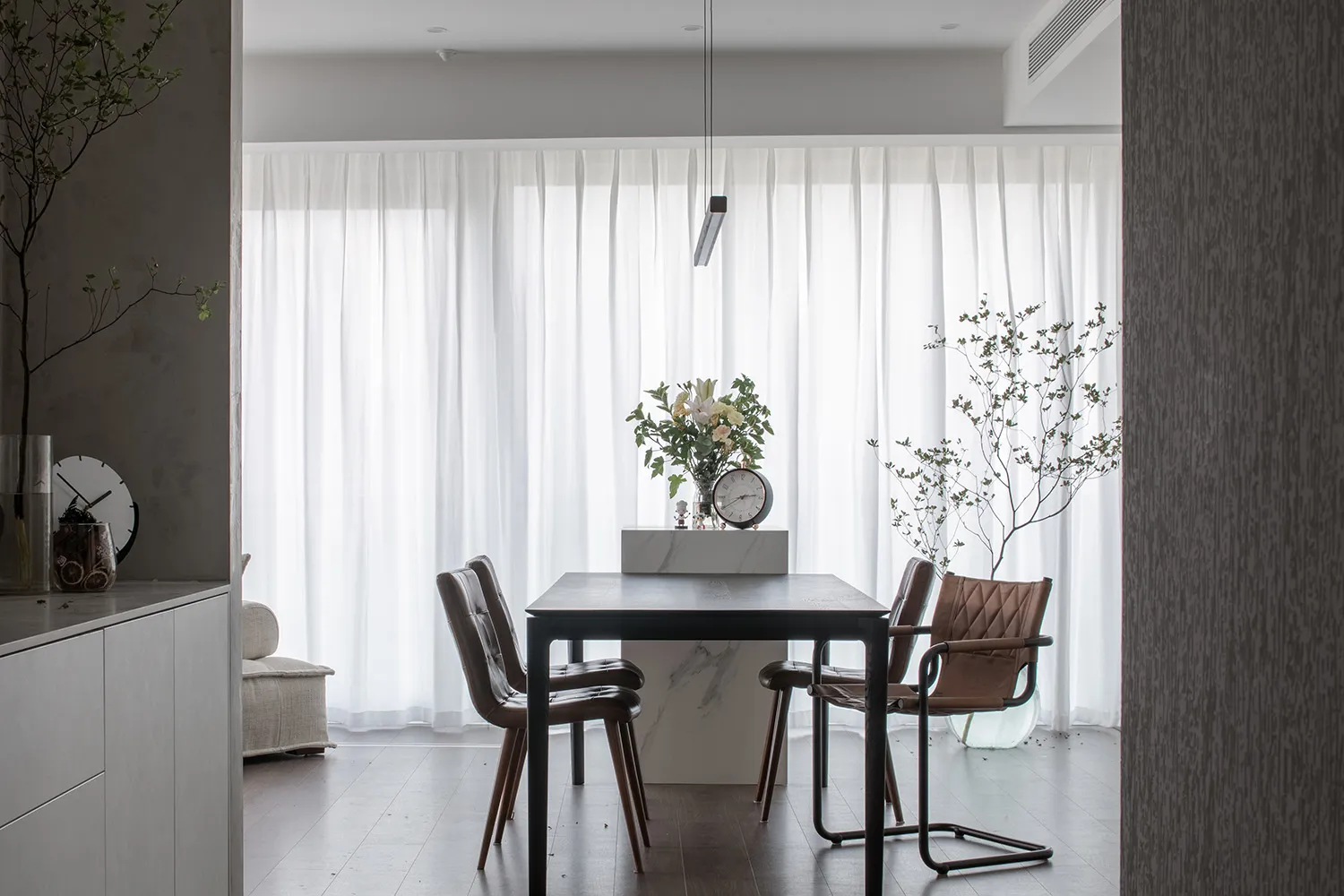 Modern minimalist dining room with white curtains, marble table, leather chairs, and indoor plants.