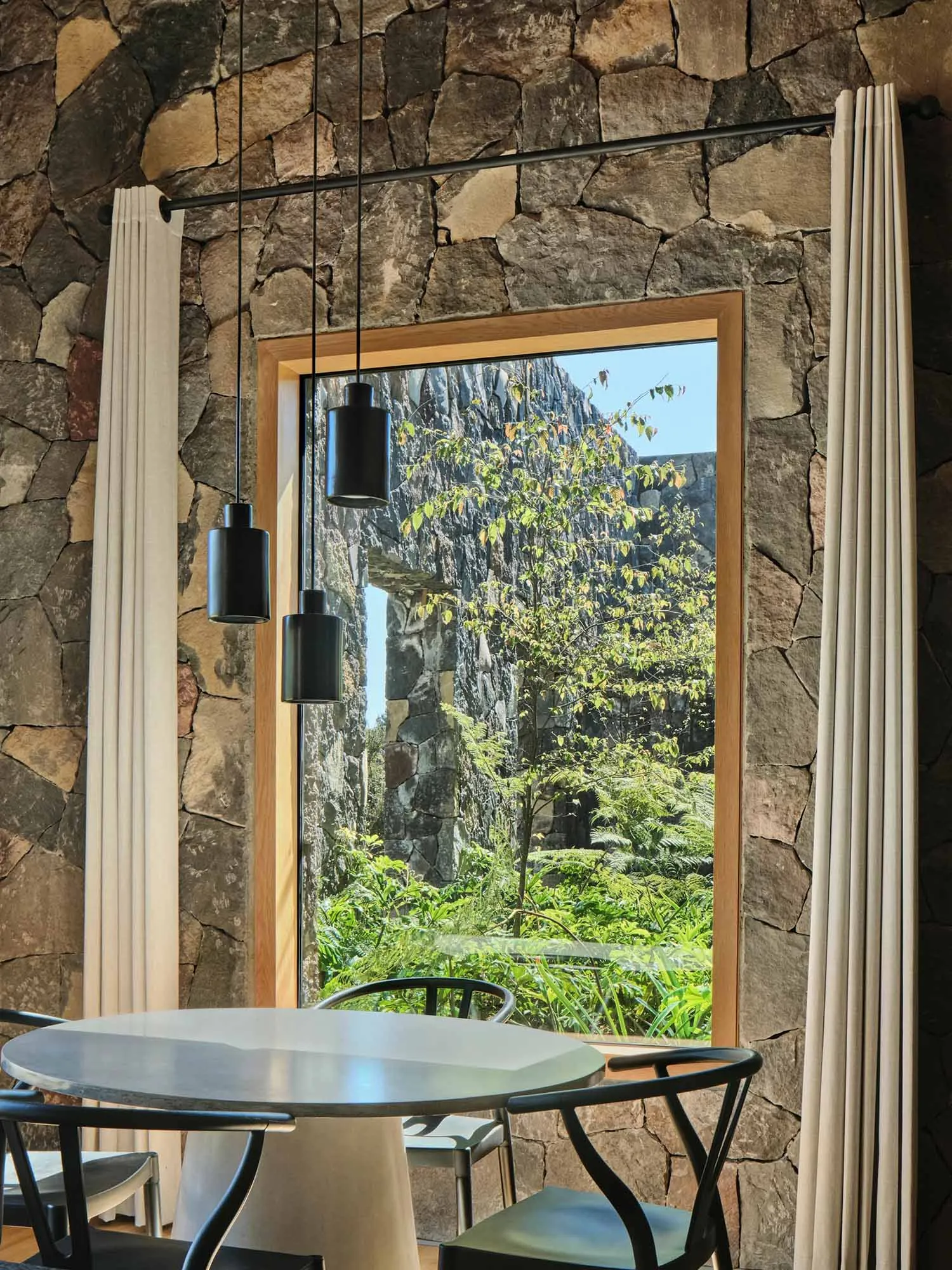 Modern dining room interior with wooden furniture, glass pendant lights, and stone walls