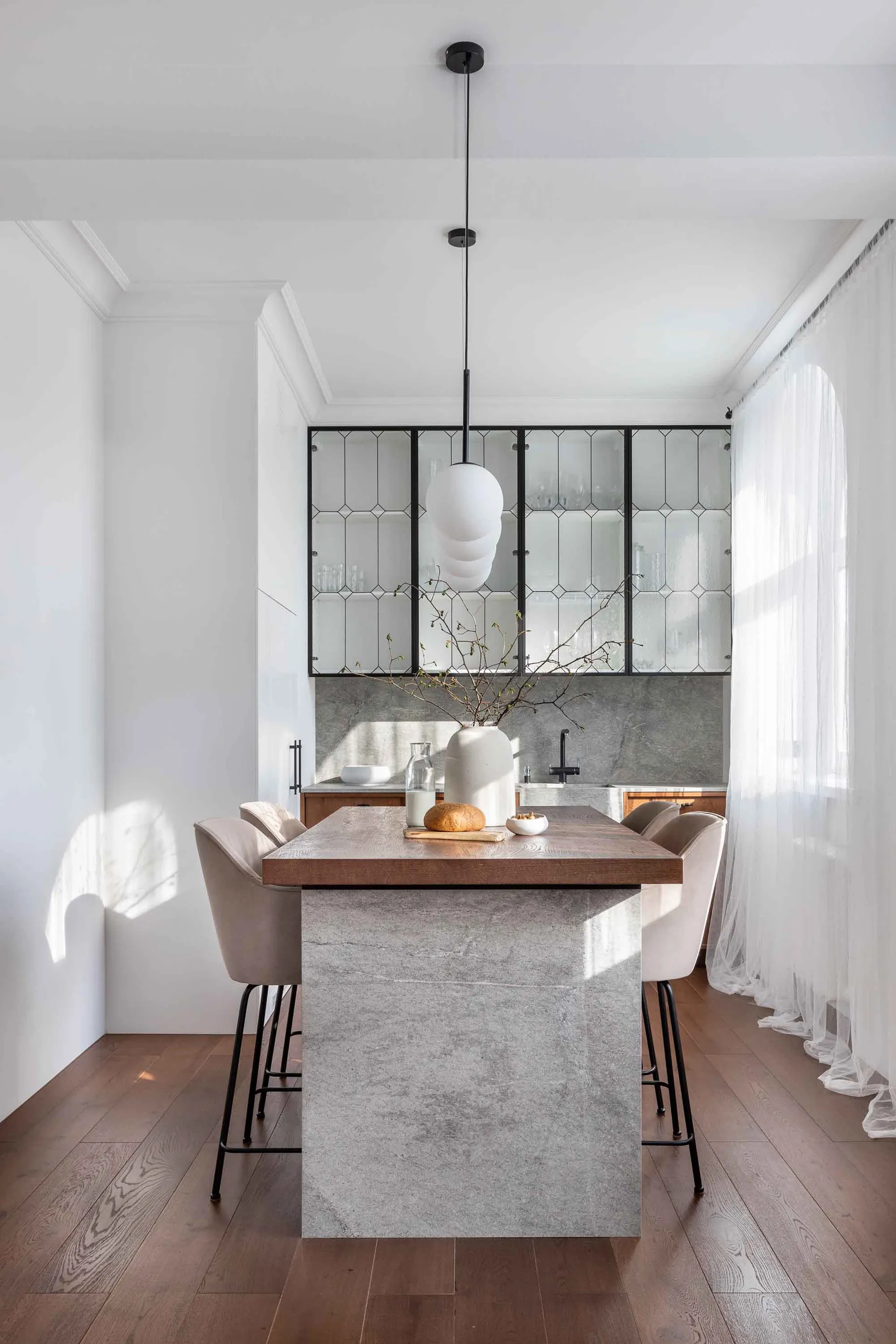 Modern kitchen with wooden dining table and concrete island, featuring a hanging pendant light and beige upholstered chairs.