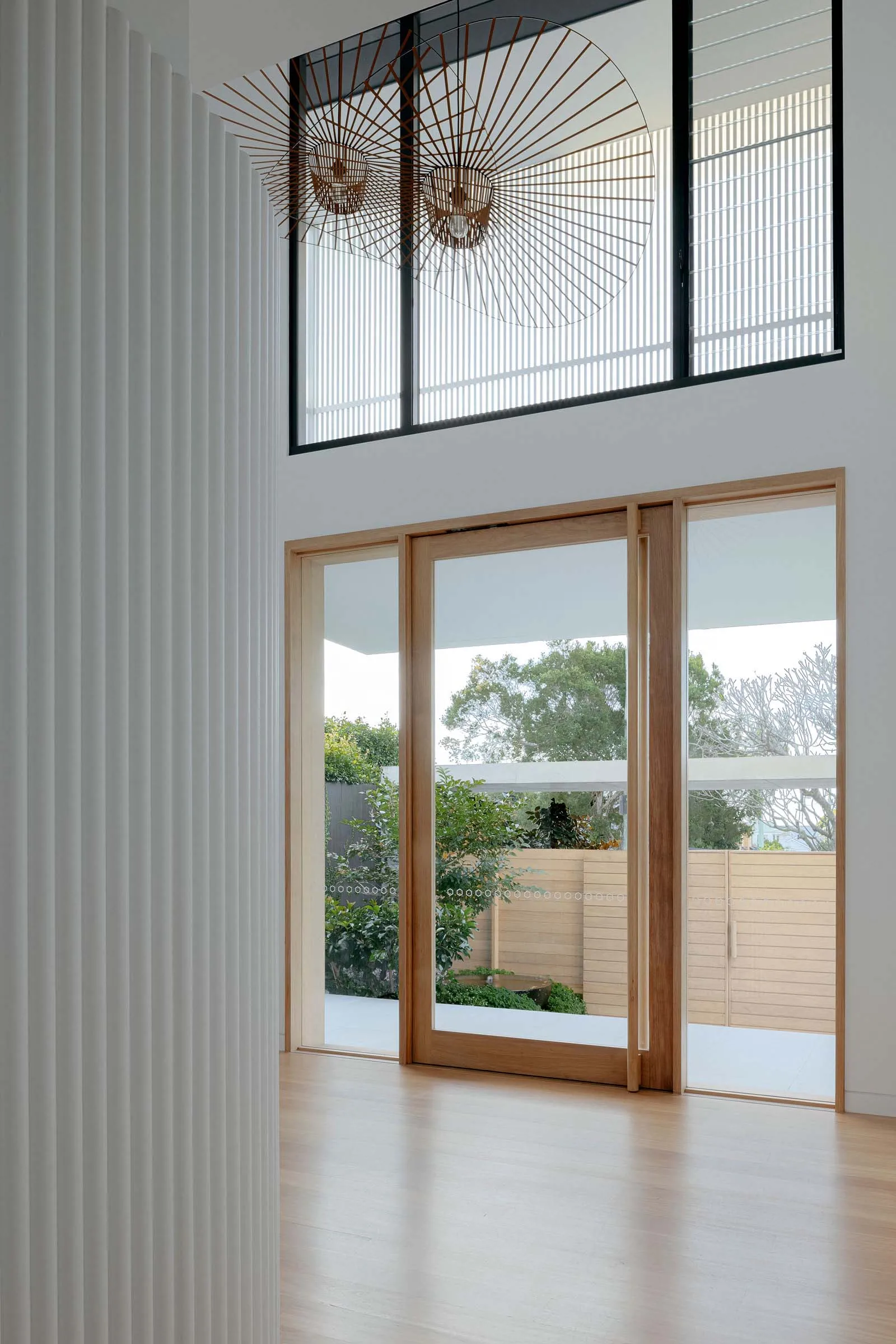 A minimalist living space featuring light-colored wood and glass doors, with a view of a green garden.